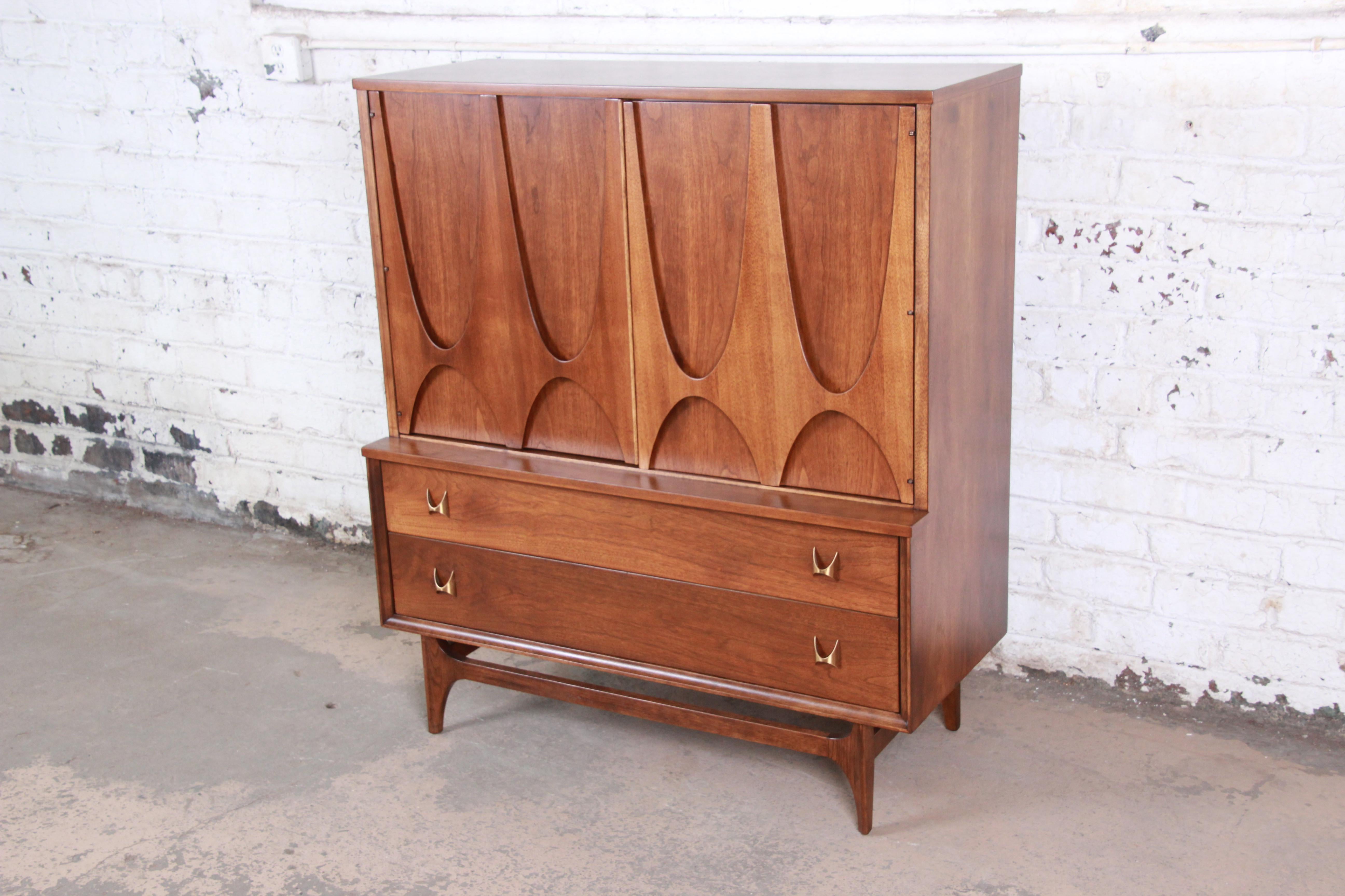 An exceptional and iconic Mid-Century Modern sculpted walnut gentleman's chest by Broyhill Brasilia. The chest has gorgeous walnut wood grain, sculpted arches, and original brass arch pulls. The two large cabinet doors open up to four dovetailed