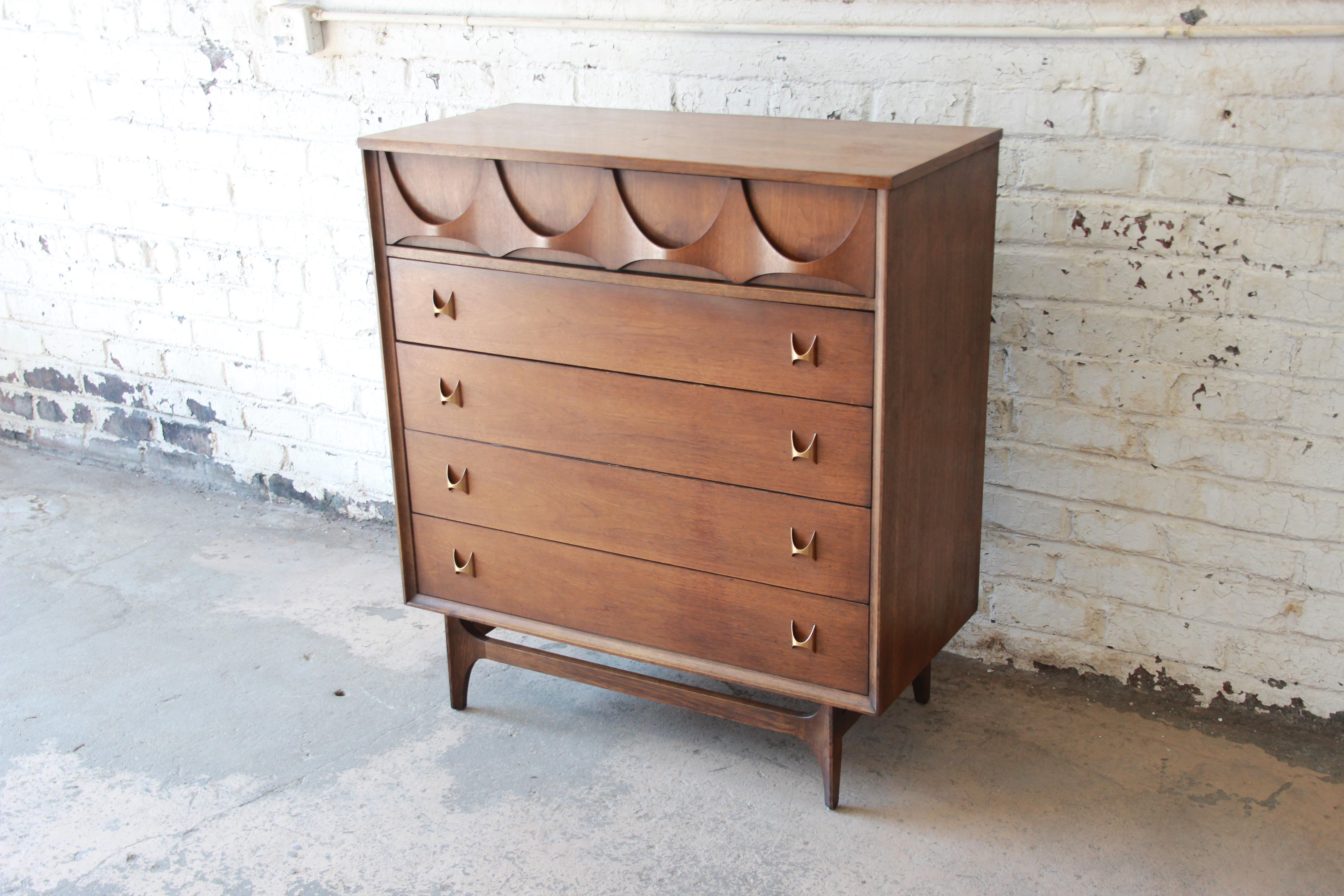 An iconic Broyhill Brasilia Mid-Century Modern sculpted walnut five-drawer highboy dresser. The dresser features gorgeous walnut wood grain, with sculpted arches and original pulls. It offers ample room for storage, with five deep dovetailed
