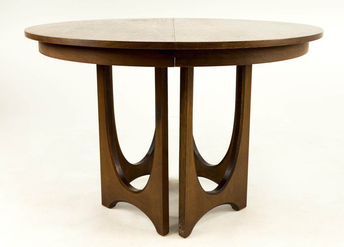 Broyhill Brasilia mid century round walnut pedestal dining table.
This table measures 44 inches in diameter and 30 inches tall, with a chair clearance of 27 inches. Included are 2 leaves that are each 12 inches wide, making the table expandable to
