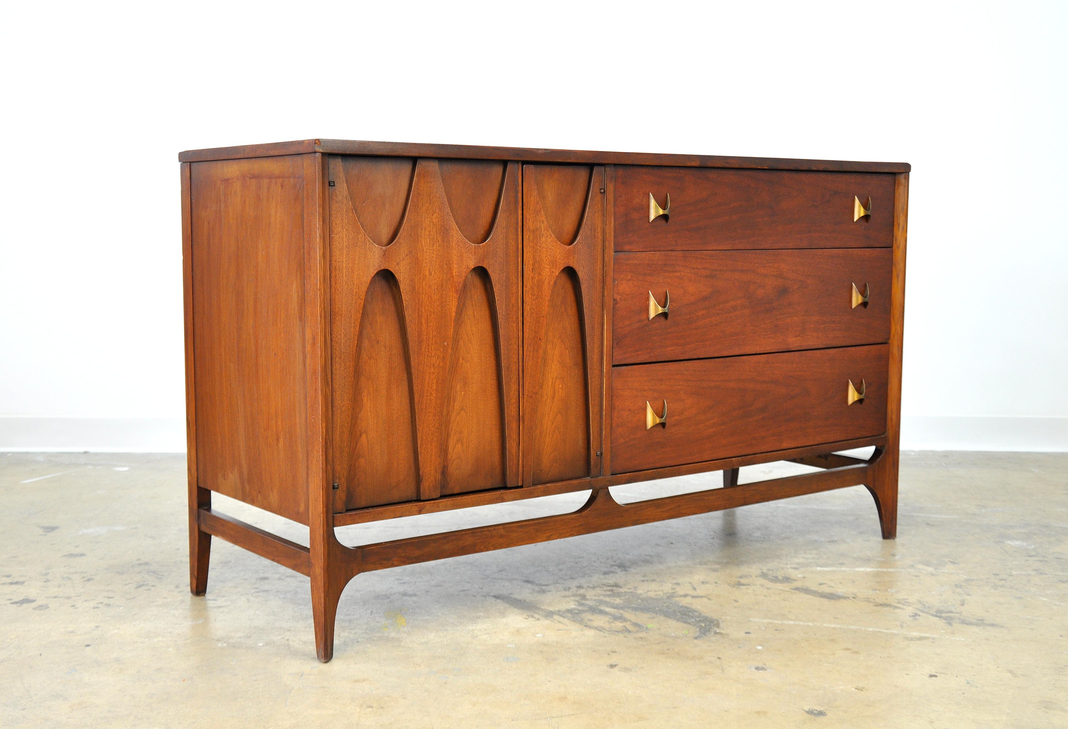 A vintage Mid-Century Modern dresser from the highly desirable Brasilia collection manufactured by Broyhill in the 1960s. The case piece, features three drawers with shaped brass pulls and cabinet doors with the signature relief cut and sculpted