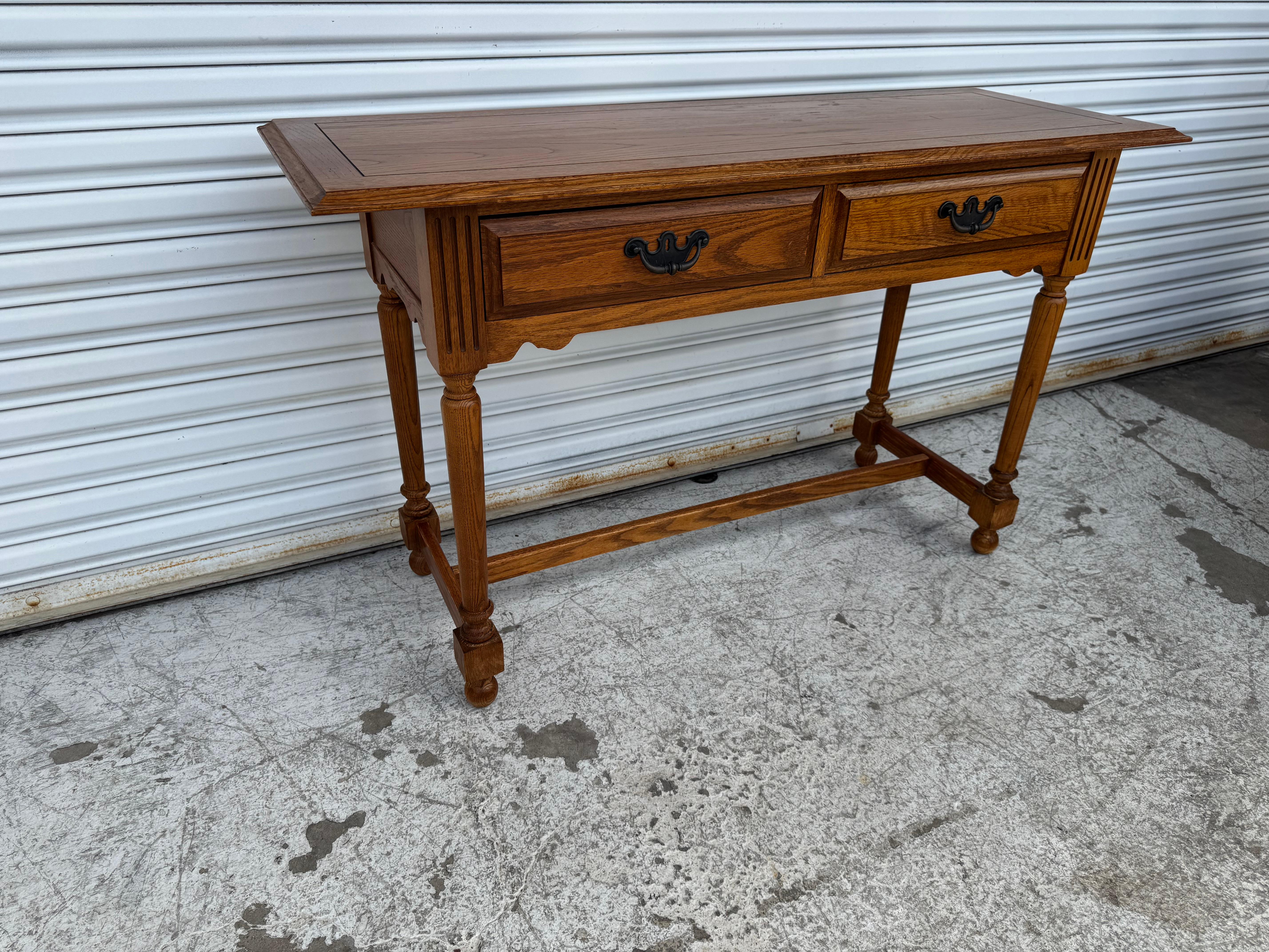 This Broyhill console table showcases timeless traditional craftsmanship with its warm oak finish, turned legs, and elegant fluted details. Featuring two spacious drawers with vintage-style brass hardware, it offers both style and storage, perfect