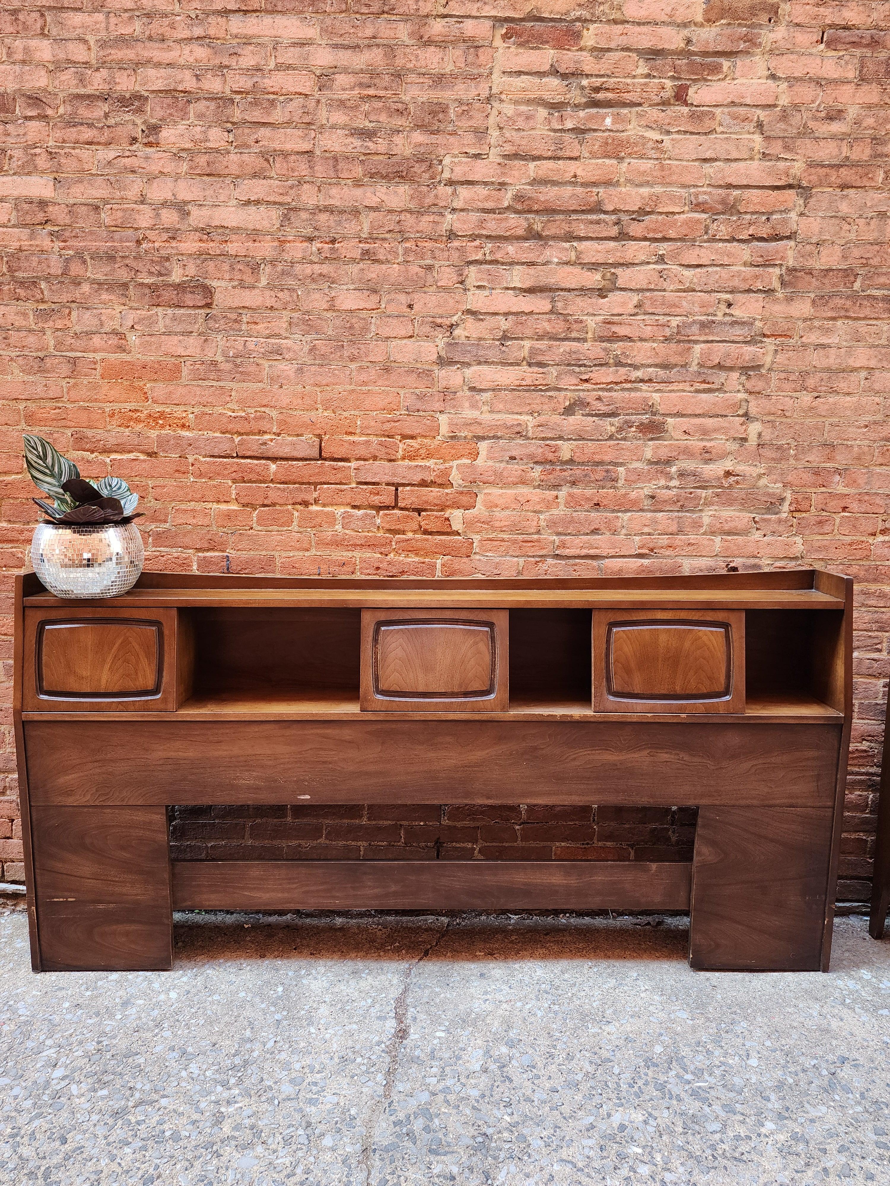 This walnut Mid-Century Modern headboard is from the Emphasis line by Broyhill. The three door panels slide to reveal a generous storage area. This headboard also has an electrical outlet installed in one compartment. 

Dimensions 80