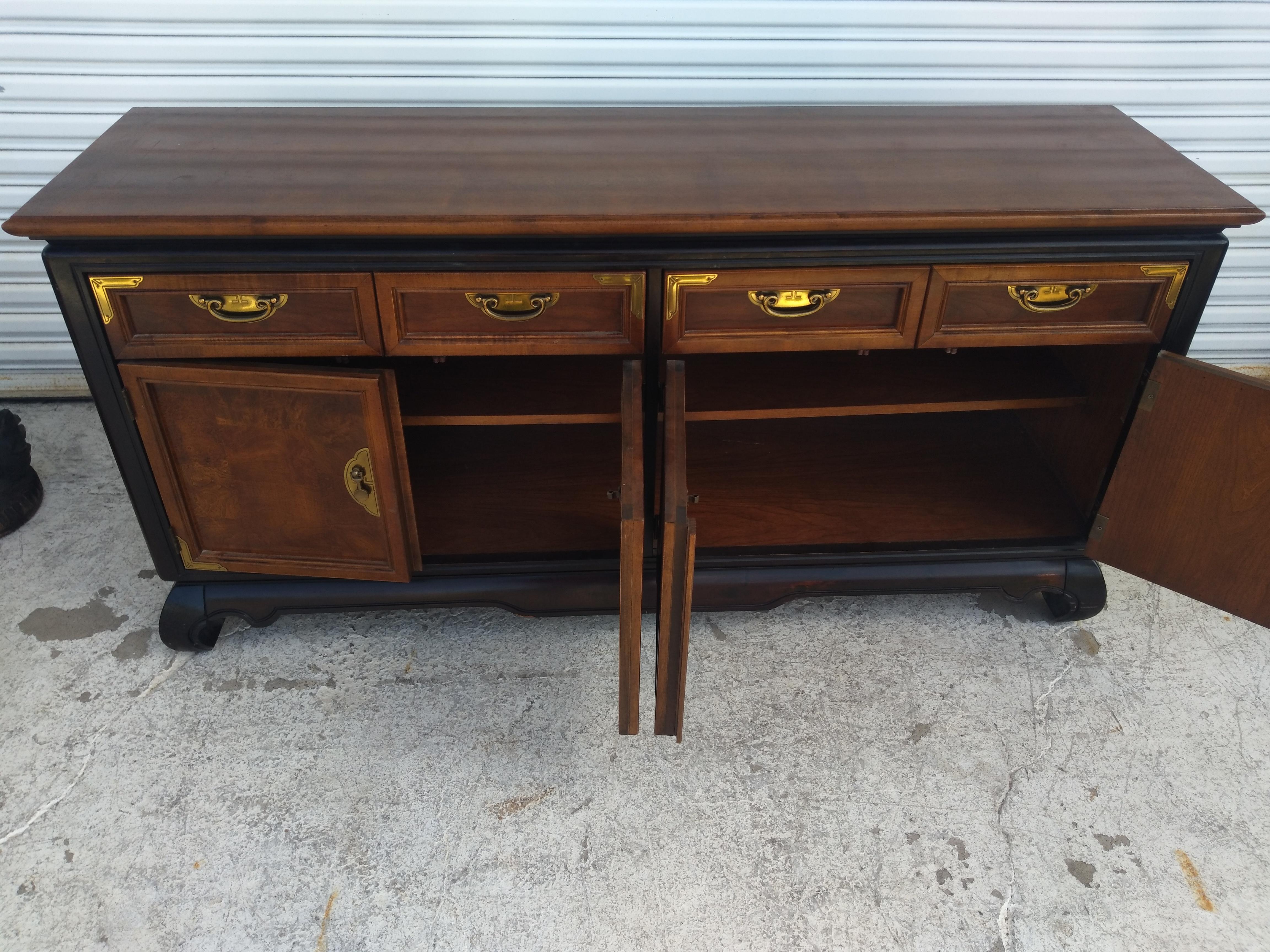 Broyhill Furniture produce mobili di buona qualità da decenni. Si tratta di un pezzo in stile Chin Hua della linea di mobili Premier. Presenta accenti e tiranti in ottone. Il legno di noce è impreziosito da accenti di ebano che lo rendono un pezzo