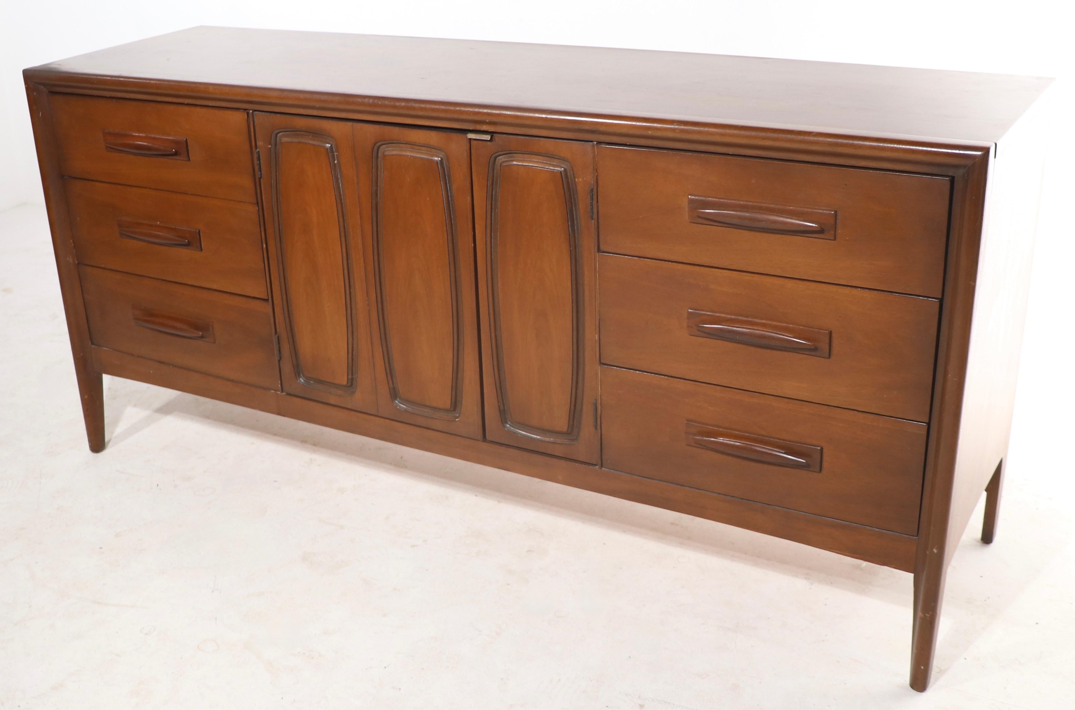 Classic American made mid century dresser, by the noted furniture company Broyhill, as part of their premier Emphasis collection. This example features two banks of drawers, each having an unusual sculpted wood pull, flanking doors which open to