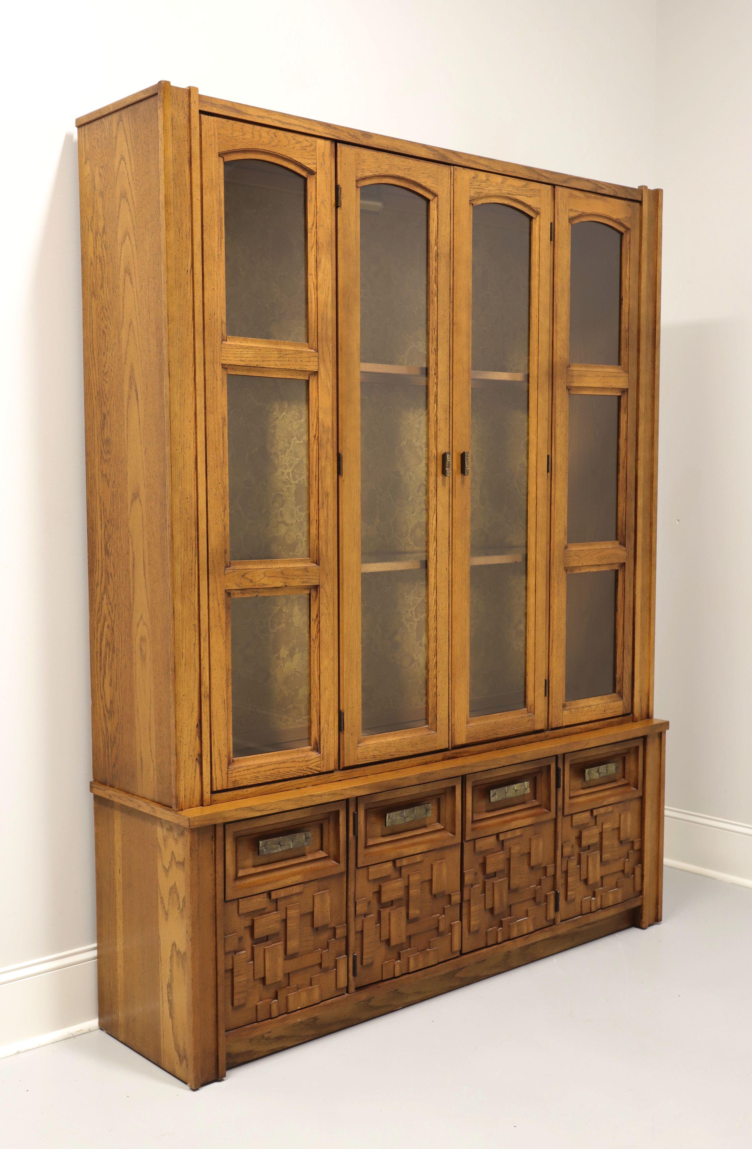 A Mid 20th Century Brutalist style china cabinet by Broyhill Premier. Oak with slightly distressed finish, oak veneers, geometric design brass hardware, raised intricately laid, highly textured, geometric design to door fronts, and on a solid base.