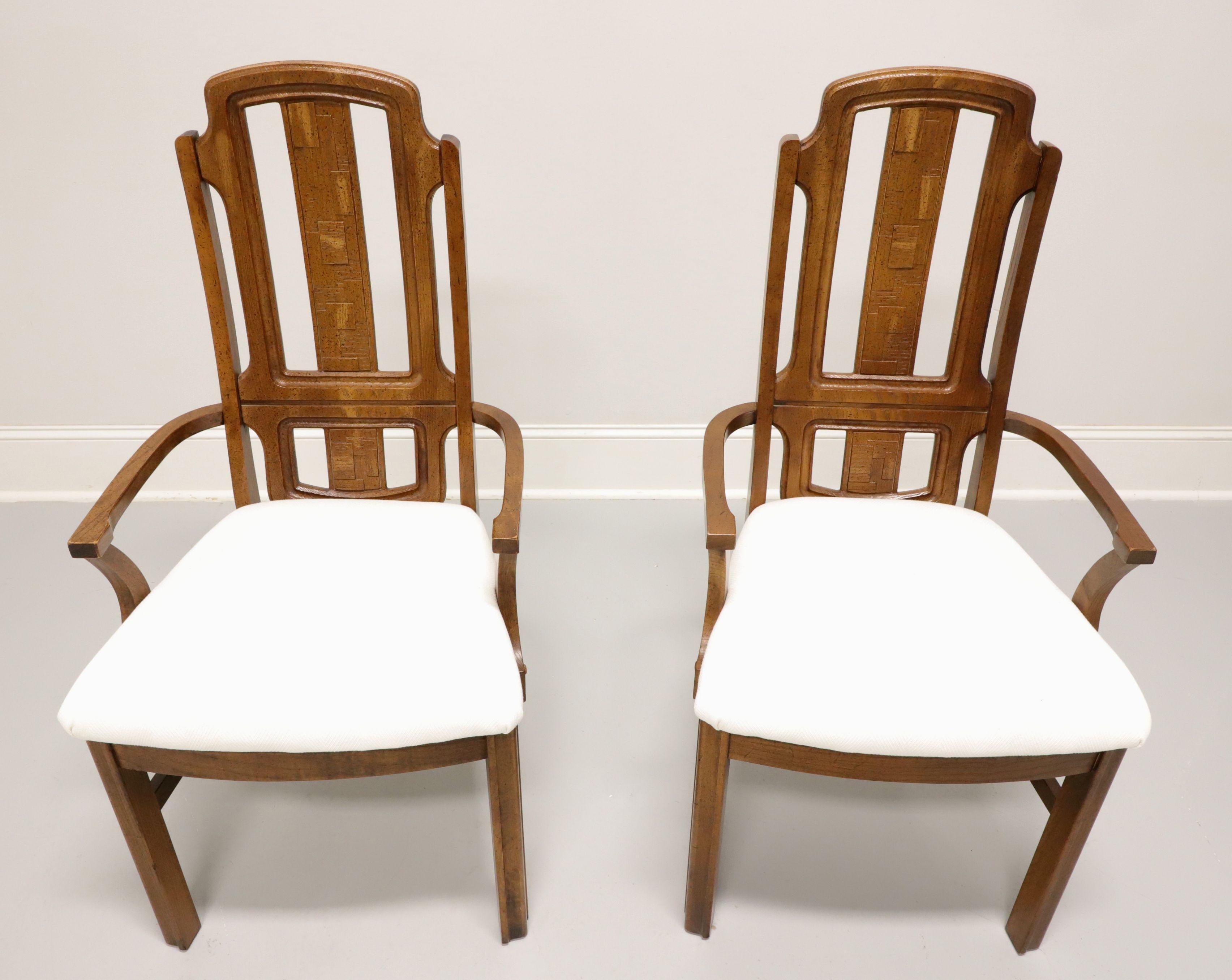 A pair of Mid 20th century Brutalist style dining armchairs by Broyhill Premier. Oak with slightly distressed finish, arched crestrail, raised & textured geometric design to backrest, gently curved arms with arched supports, neutral cream color