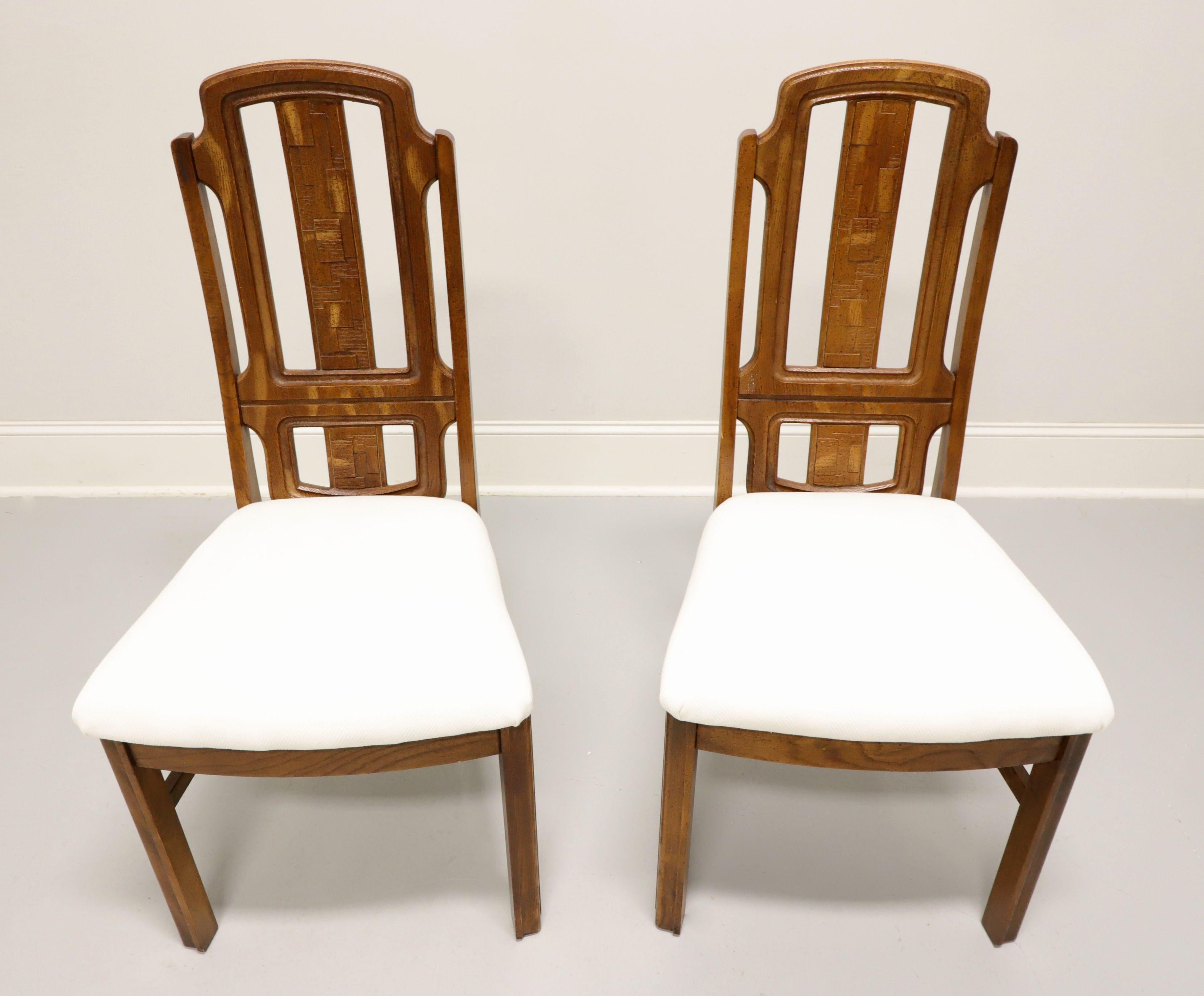 A pair of Mid 20th Century Brutalist style dining side chairs by Broyhill Premier. Oak with slightly distressed finish, arched crestrail, raised & textured geometric design to backrest, neutral cream color fabric upholstered seat, stretchers, and