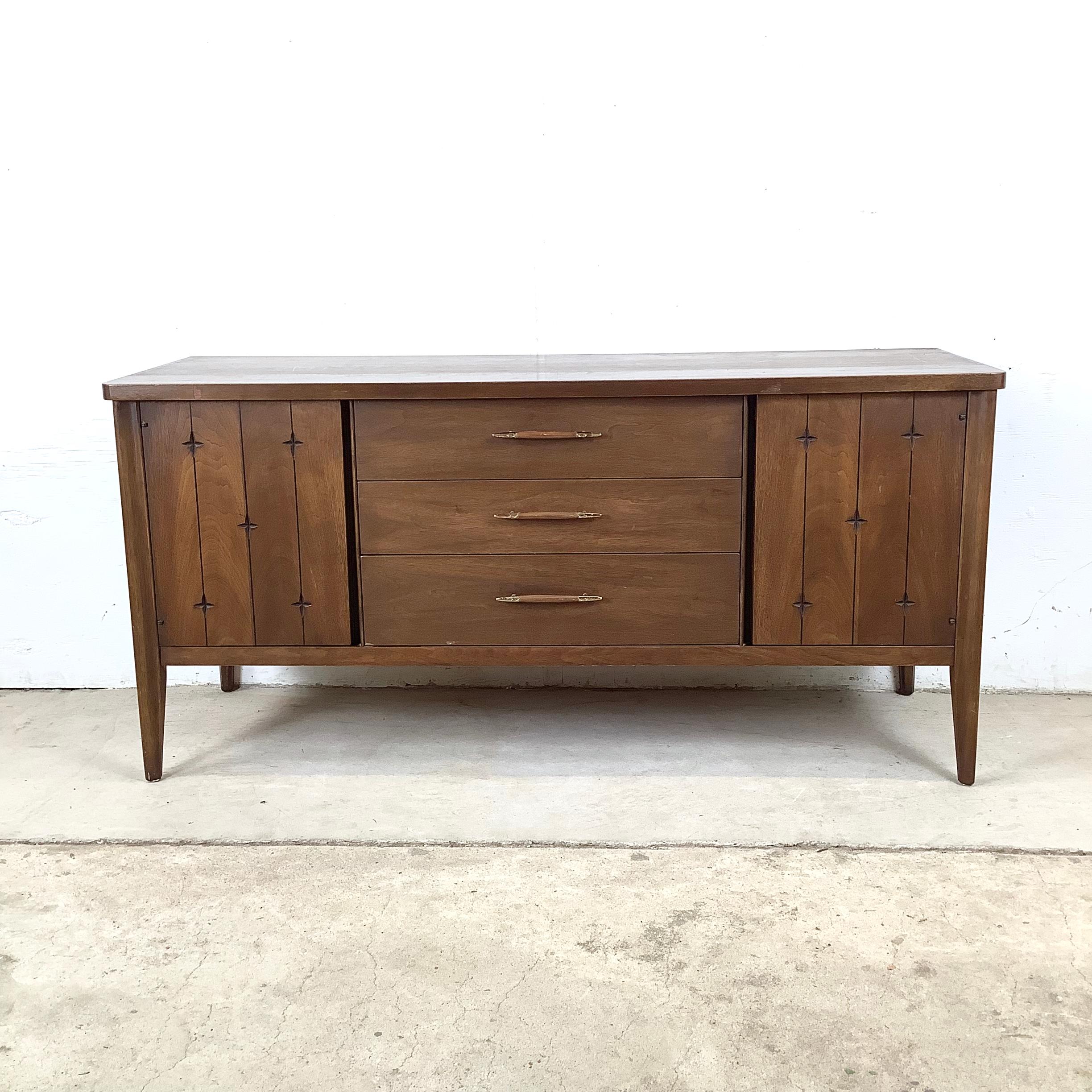 A striking example of American mid-century modern design, this two-piece china cabinet from Broyhill’s celebrated Saga collection captures the bold yet refined aesthetic of the early 1960s. Crafted in rich walnut, the cabinet features the line’s