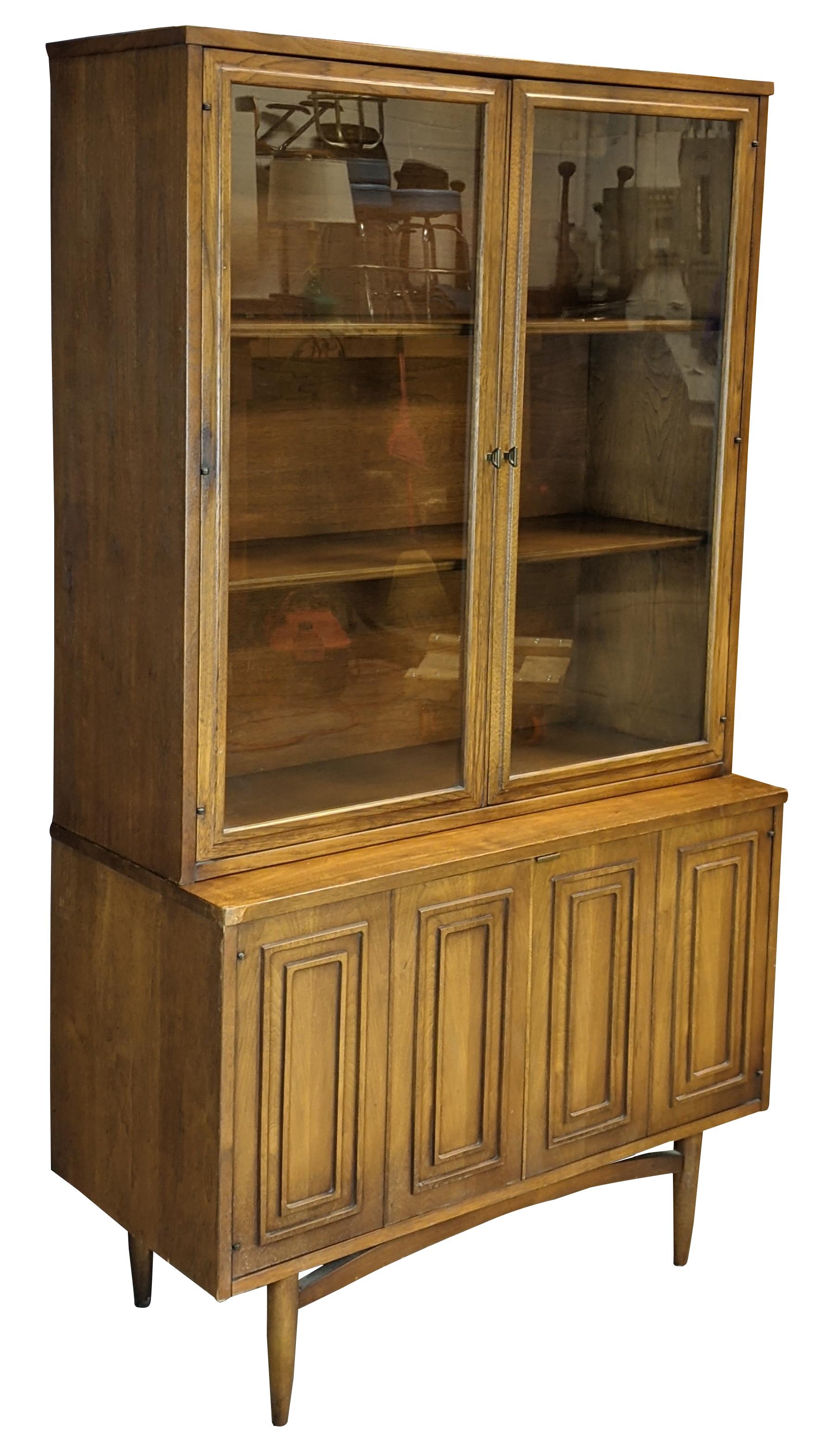 Broyhill Premier Sculptra collection bookcase or china cabinet, circa 1960s. Made of walnut with Mid-Century Modern styling. Tapered legs support a two-door compartment with inner drawer, and two glass doors open to three shelves.

Measures: 17