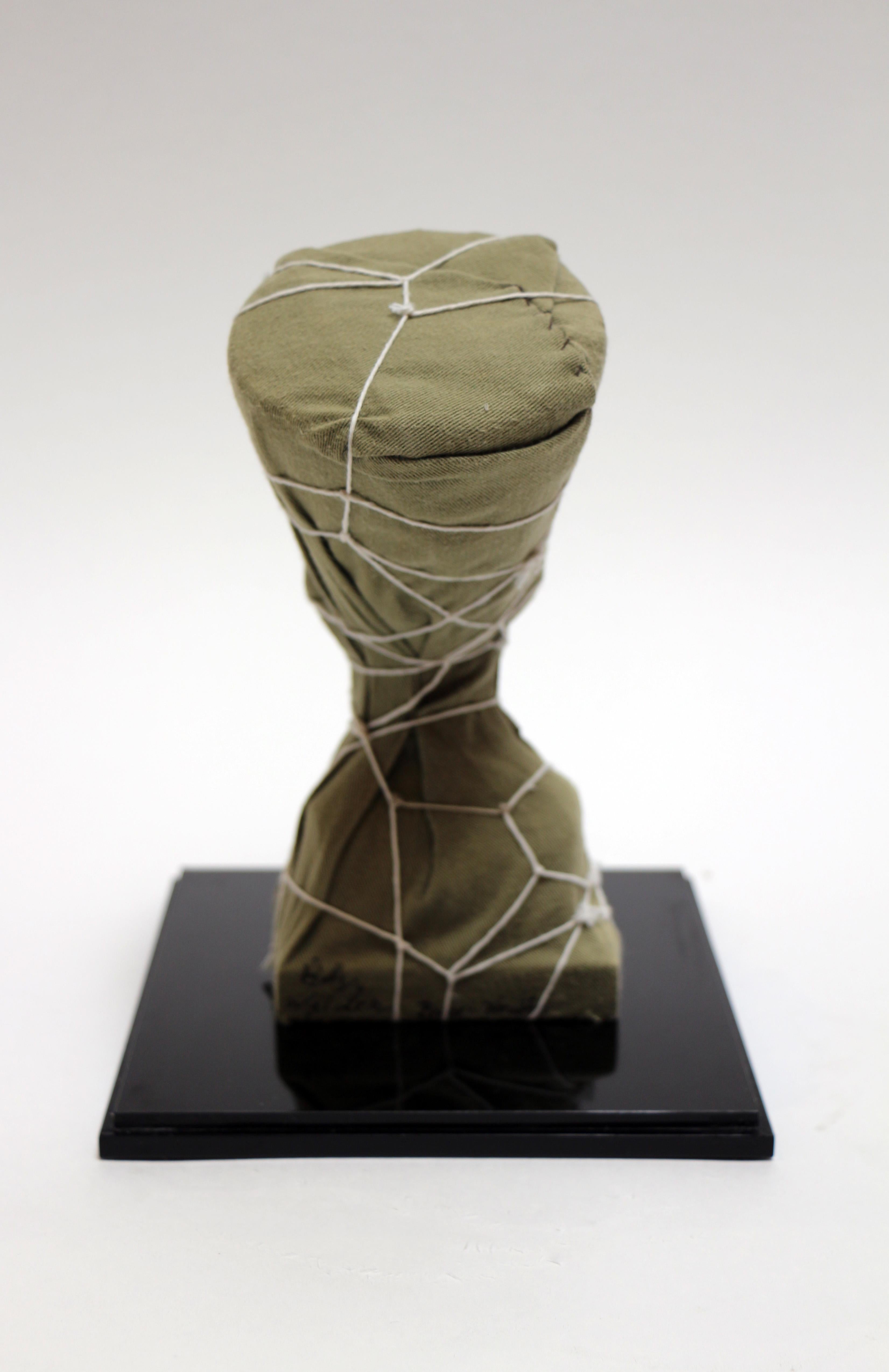 This statue is a depiction of Nefertete in Christo themed attire with an army green cloth covering the entirety of the statue and tied with string. The work is a collaboration between artists Billy Wilder and Bruce Houston. 

Billy Wilder