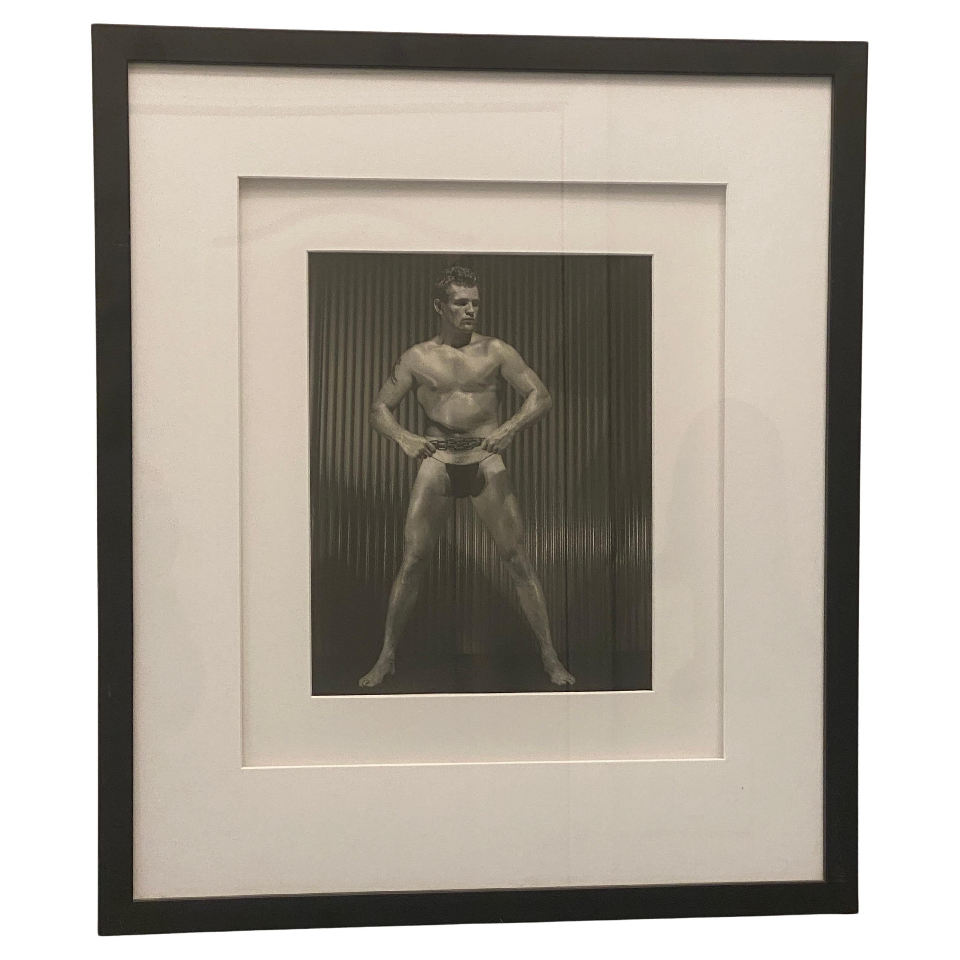 Issue d'une importante collection de photographies de physique masculin et d'Icone datant de plus de 25 ans, cette image emblématique d'un modèle masculin tenant une chaîne en métal... Imprimées dans les années 1960, elles sont toutes signées par le