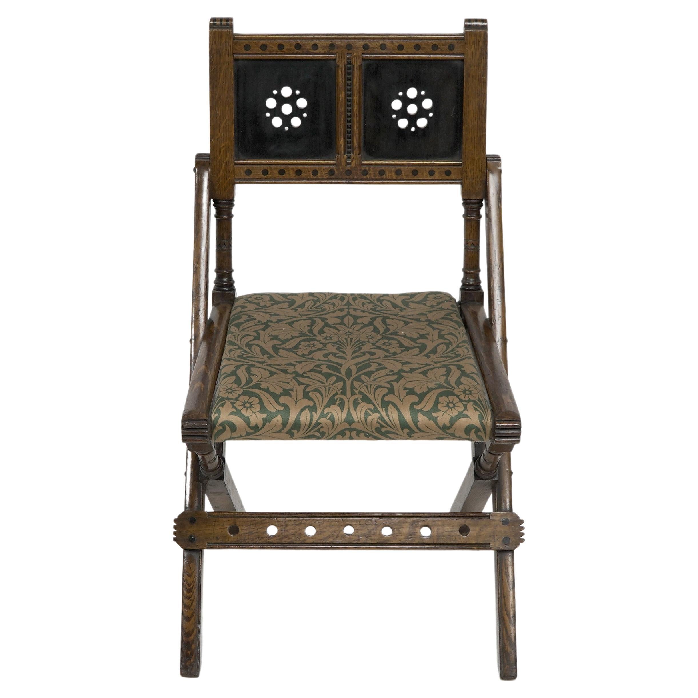 Bruce Talbert for Gillows and Co. An Aesthetic Movement scissor style side chair with ebonized dot details and chip carved details to the frame, the back panels with ebonized through circular decoration to the centres, with chevron carved details to