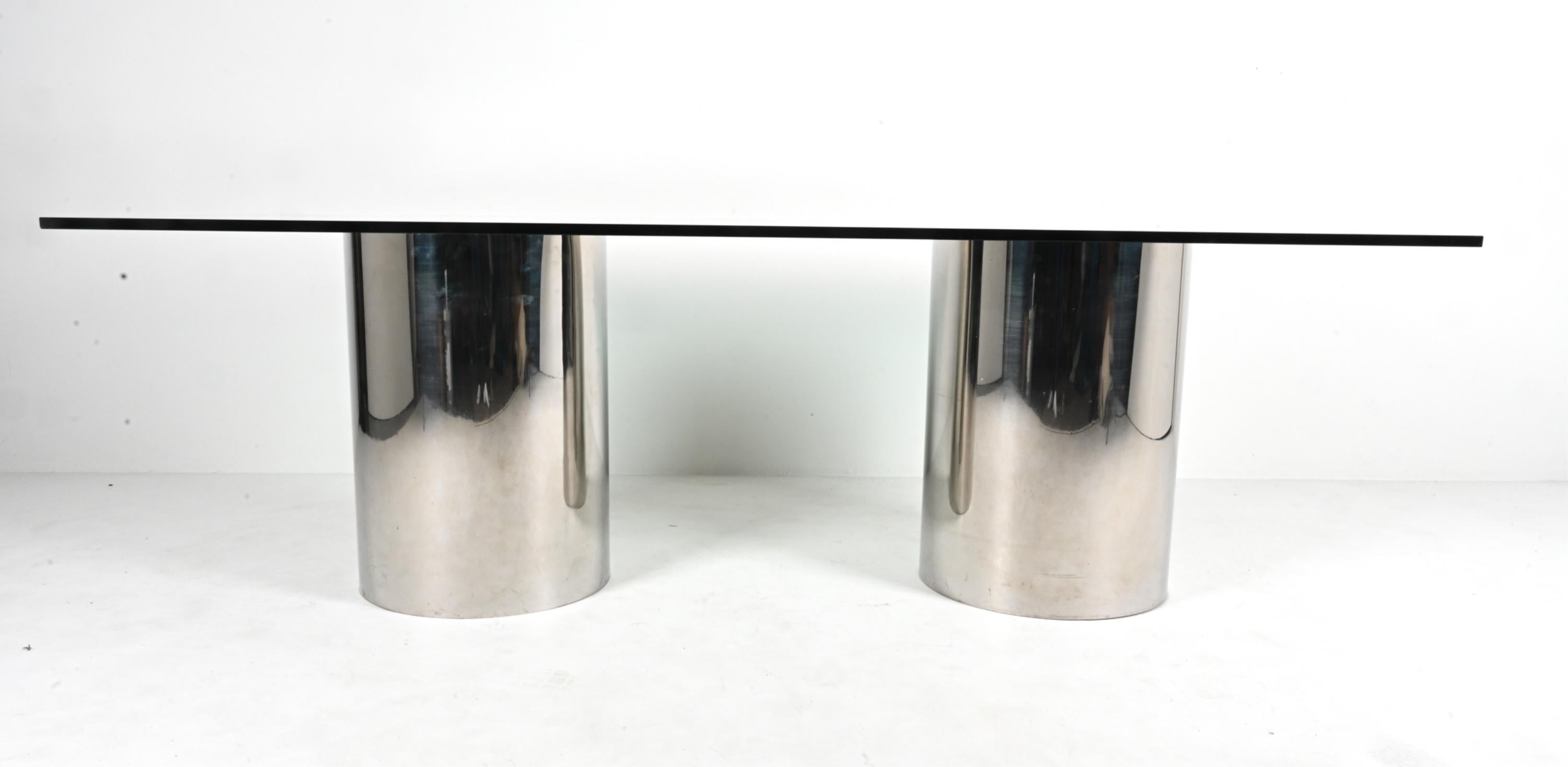 Exemplaire de l'élégance moderne minimaliste, cette rare table de salle à manger documentée de la série Drum de Brueton présente un plateau rectangulaire en verre trempé soutenu par deux piédestaux cylindriques en pin robuste, revêtus d'acier