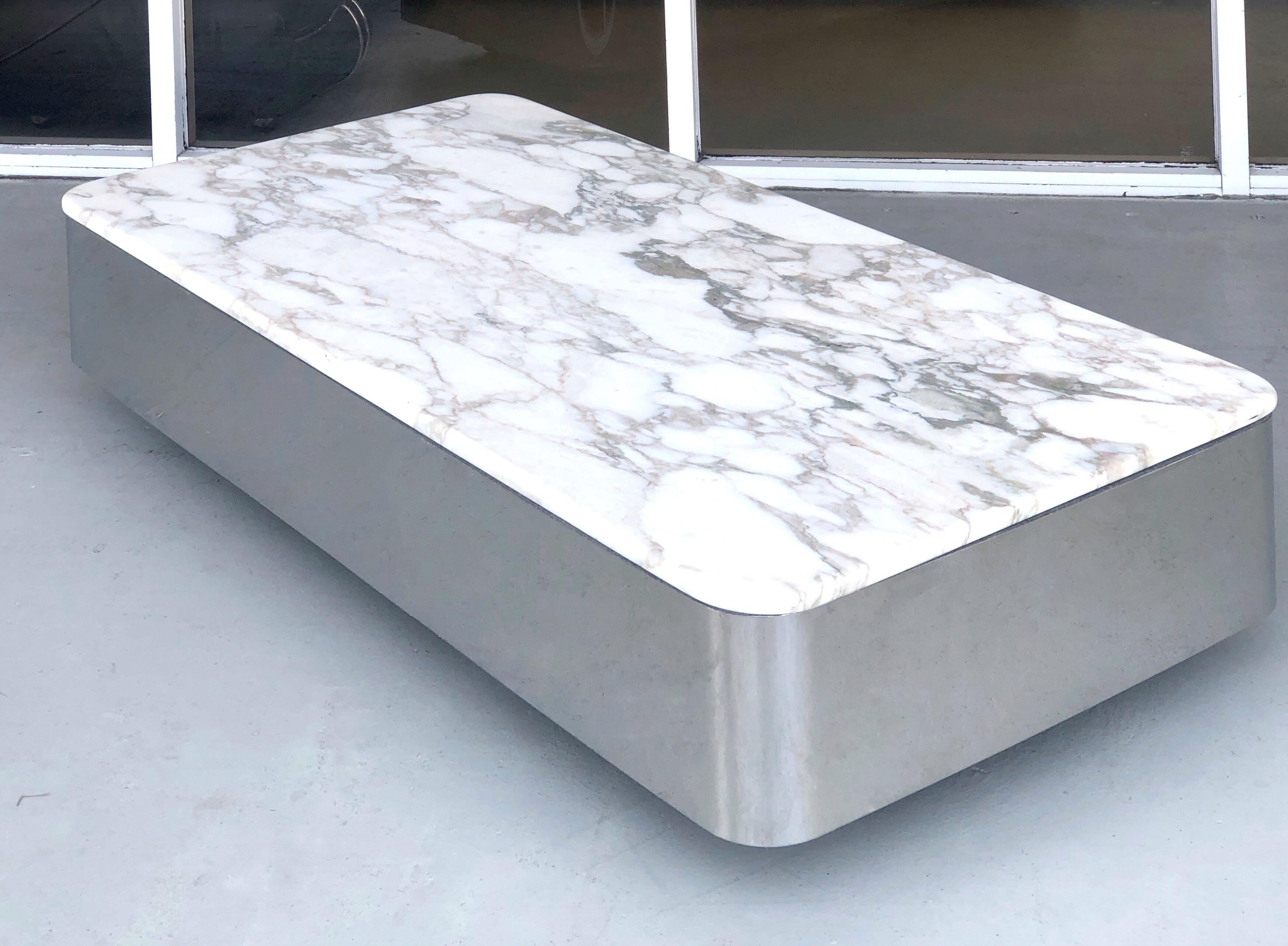 A low floating coffee table by Brueton. Polished stainless steel with a thick honed marble top. It is on casters for easy mobility, table seems to levitate.