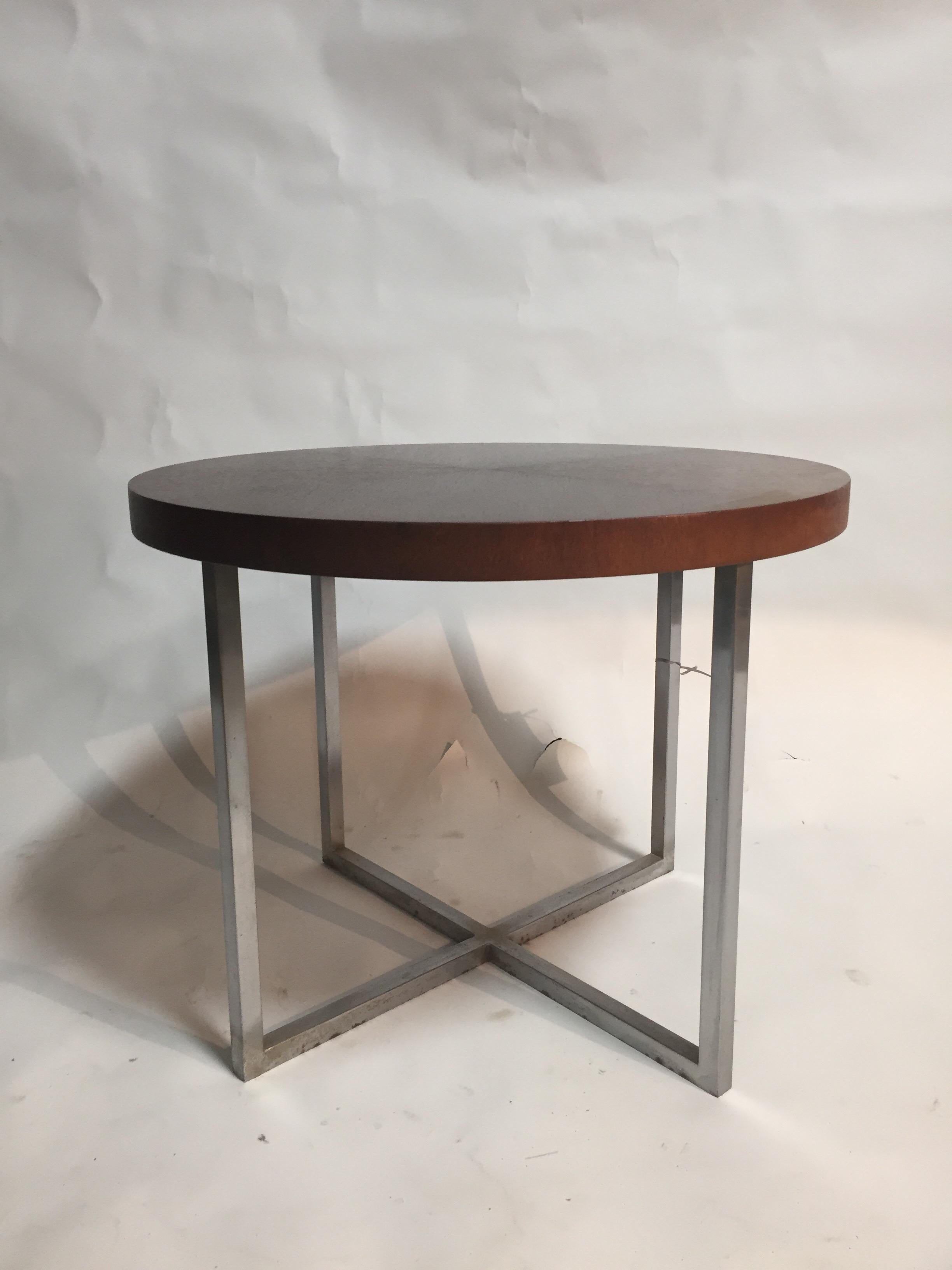 An end table with round wood top and crossed metal base by Brueton. USA, circa 1970.

A medium brown stained wood top resting on chrome finished legs.

Dimensions: 27 inches W x 21 inches H.