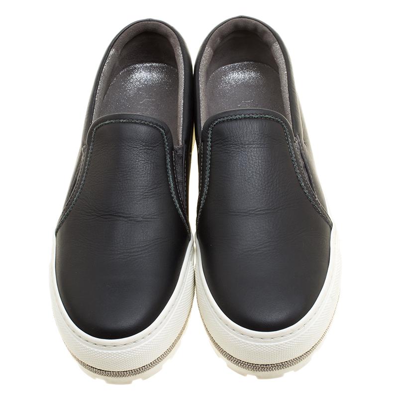 Look effortlessly stylish and sporty while being at ease through the day wearing these Brunello Cucinelli slip on sneakers. Designed in classic black leather with a thick white rubber sole, these shoes are made special with silver tone chain