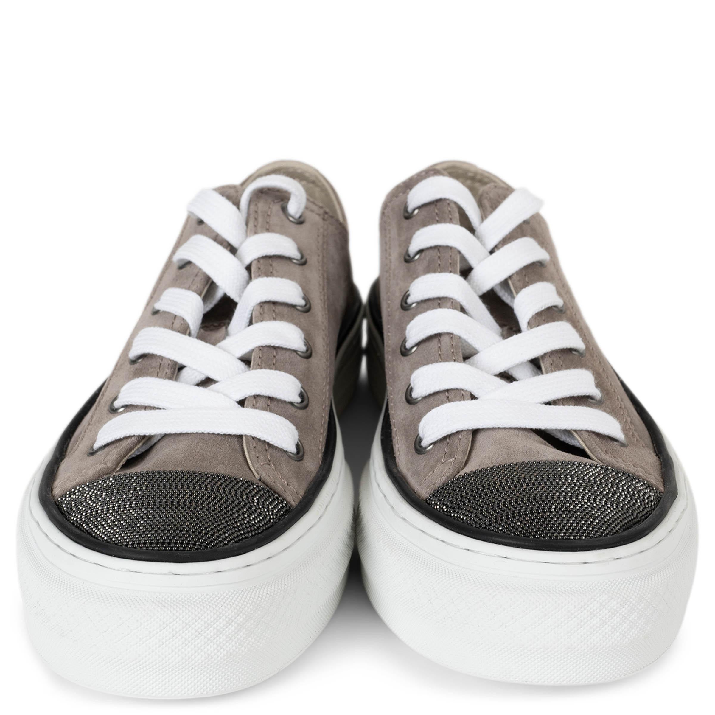 Cette paire de baskets 100 % authentique Brunello Cucinelli est réalisée en daim taupe et se distingue par un embout incrusté de Monili en bronze, qui ajoute un éclat raffiné à son design sportif. Dotées de bouts ronds avec un subtil liseré noir,