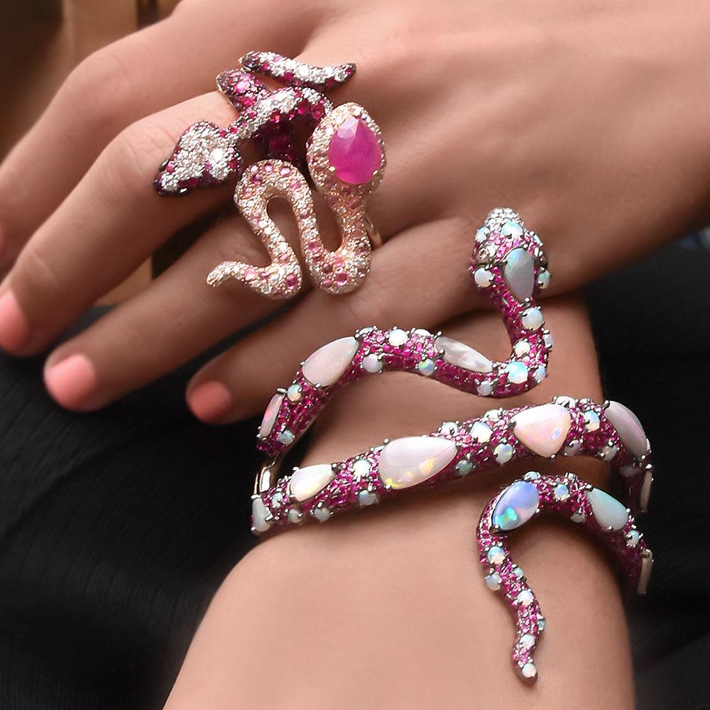 This stunning ring designed by Bruno Crivelli is a detailed 18 karat rose gold snake ring which is set with 3.08 carats of rubies, 1.15 carats of white diamonds, .05 carats of black diamonds, and 2.62 carats of amethyst. This ring measures 1.5