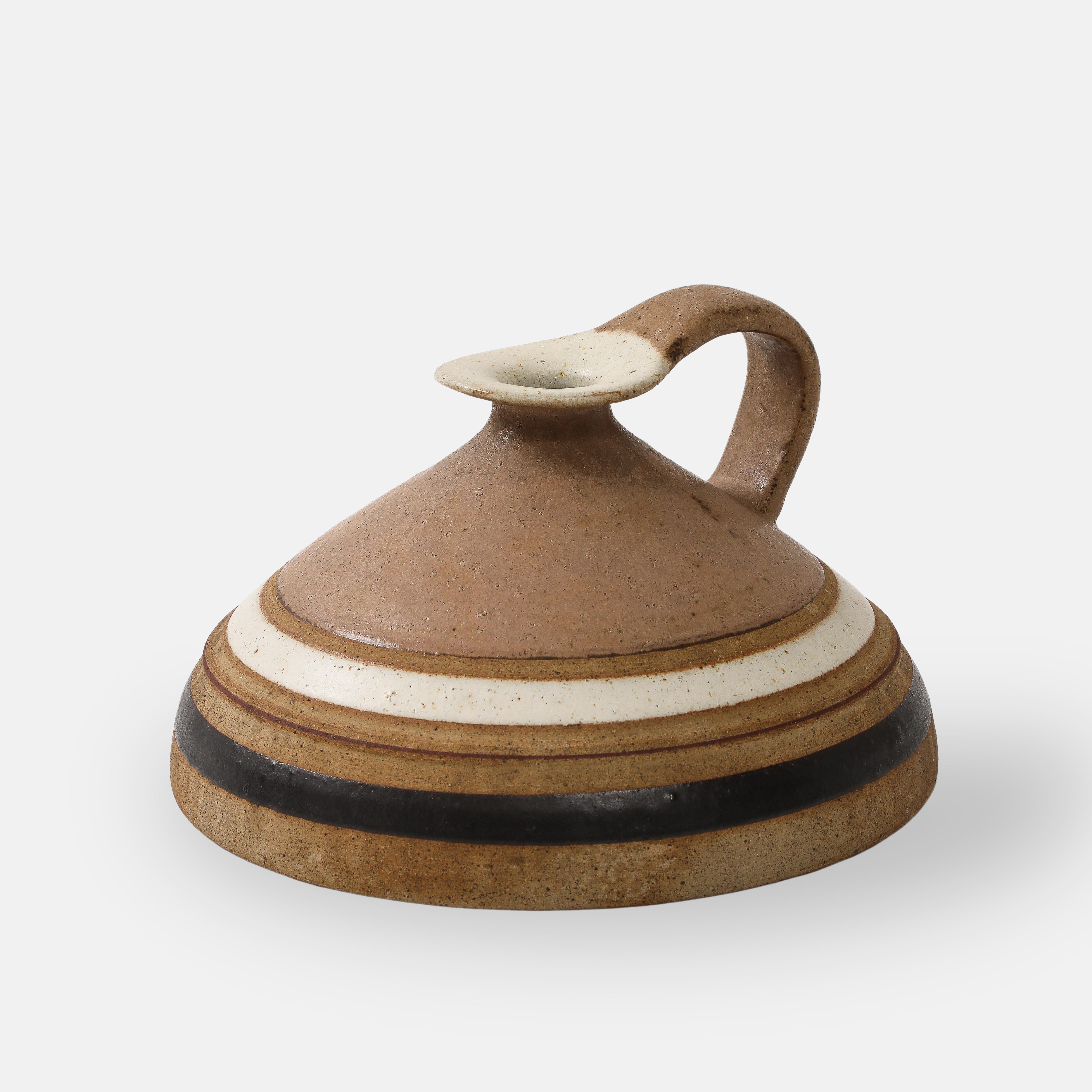 Pichet ou cruche en céramique de Bruno Gambone avec anse en glaçure fauve ou camel comprenant des bandes de  blanc cassé et brun foncé.
Signé en dessous 