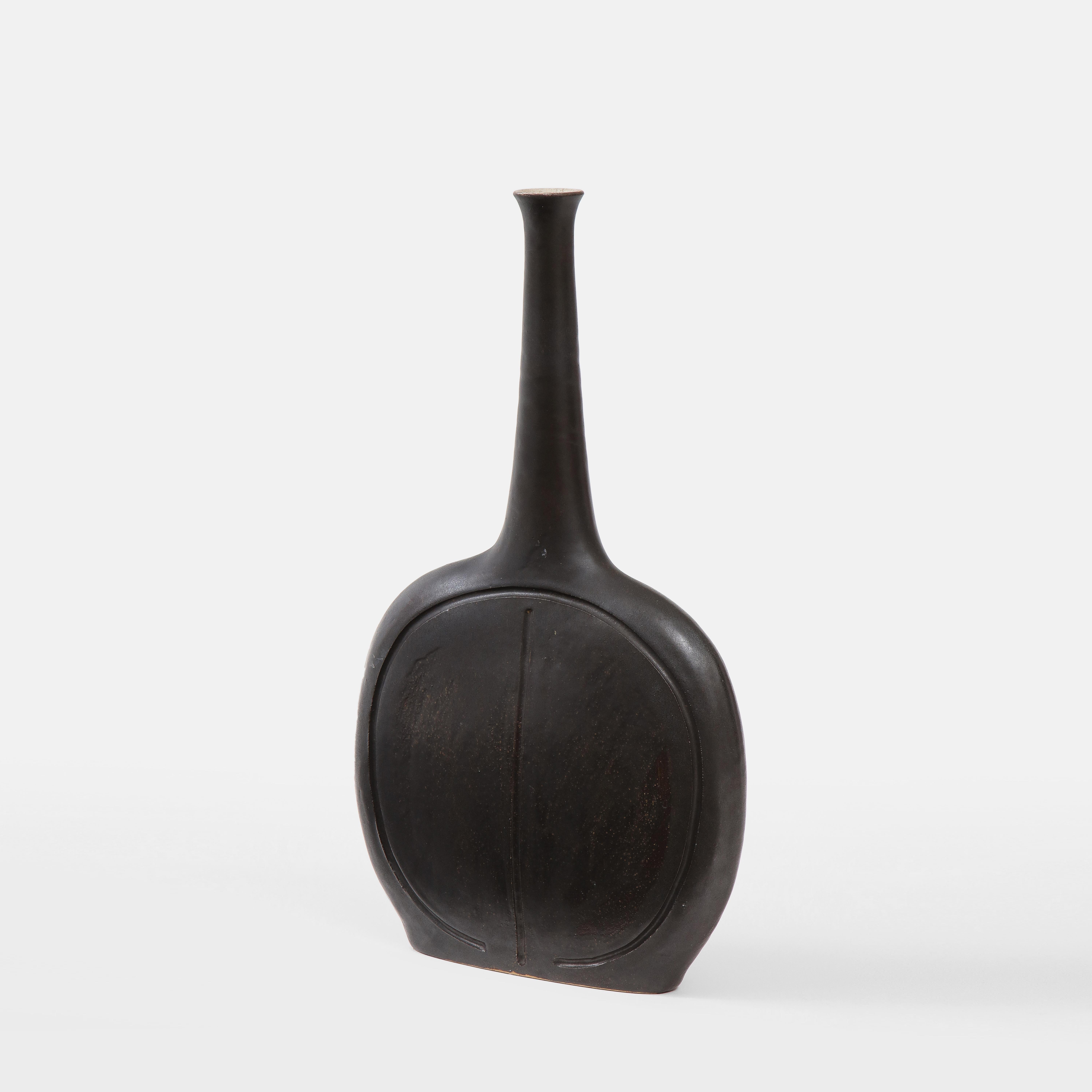 Bruno Gambone Hellschwarz glasierte Keramikflasche oder Vase mit abgeflachten kreisförmigen Körper und länglichem, sich verjüngendem Hals, Italien 1970er Jahre. Der Korpus ist mit einer abstrakten, gravierten Verzierung versehen. Signiert unten