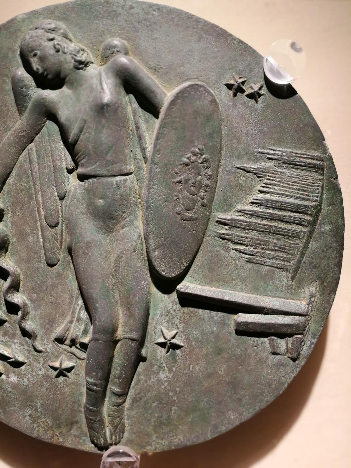 Ce relief en bronze ( 29 x 29 cm, socle en plexiglas 41 x 41 cm) est un modèle pour une médaille commémorative dédiée à l'armée de l'air italienne. 
Au centre se trouve l'Allégorie de l'armée de l'air italienne - représentée comme une femme volante