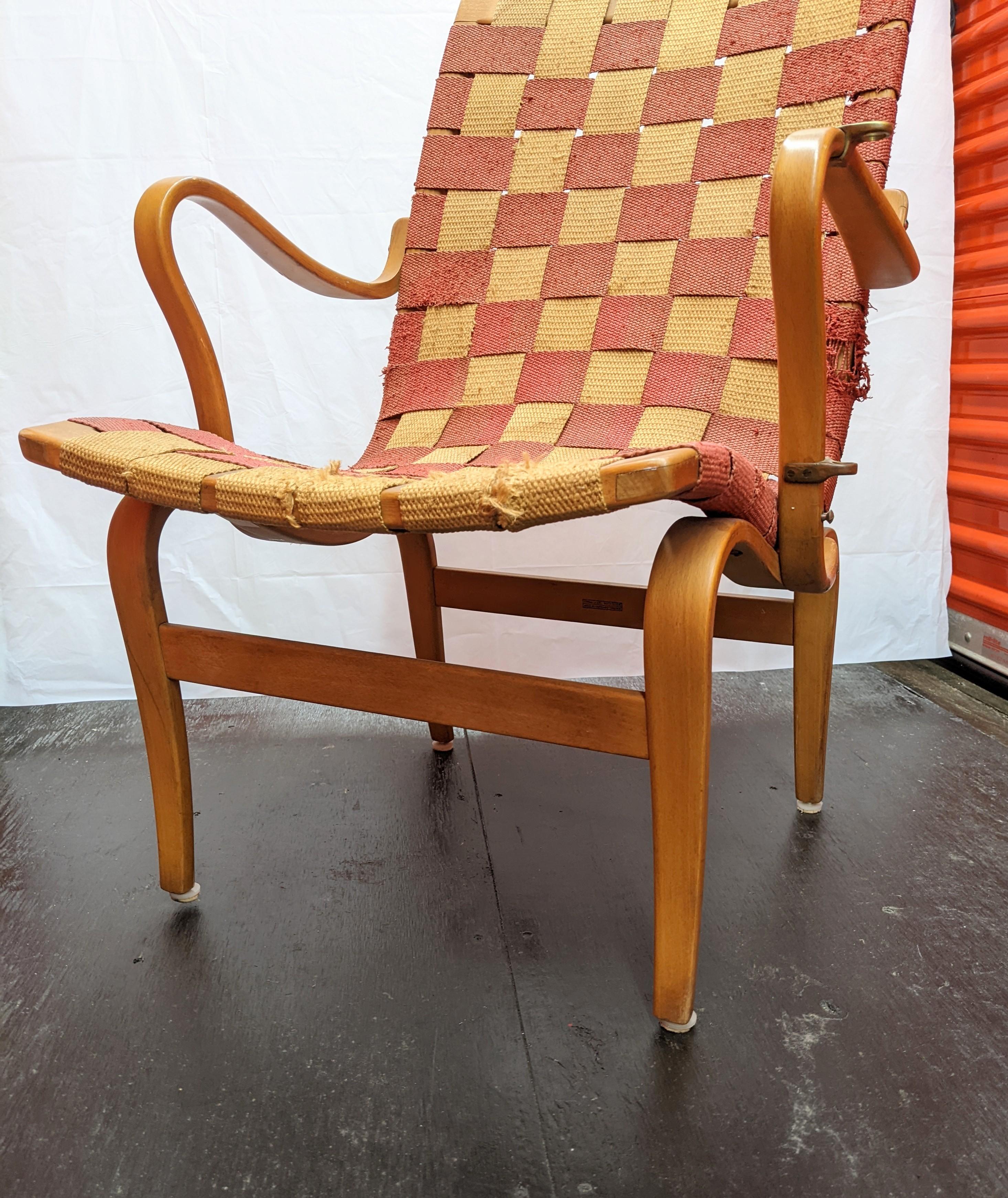 Bruno Mathsson reading chair, originally designed in 1934 in laminated beech bent wood with linen webbing. This later version has original webbing and is in worn original condition. Wood reading tray is missing but hardware is attached to arm rest.
