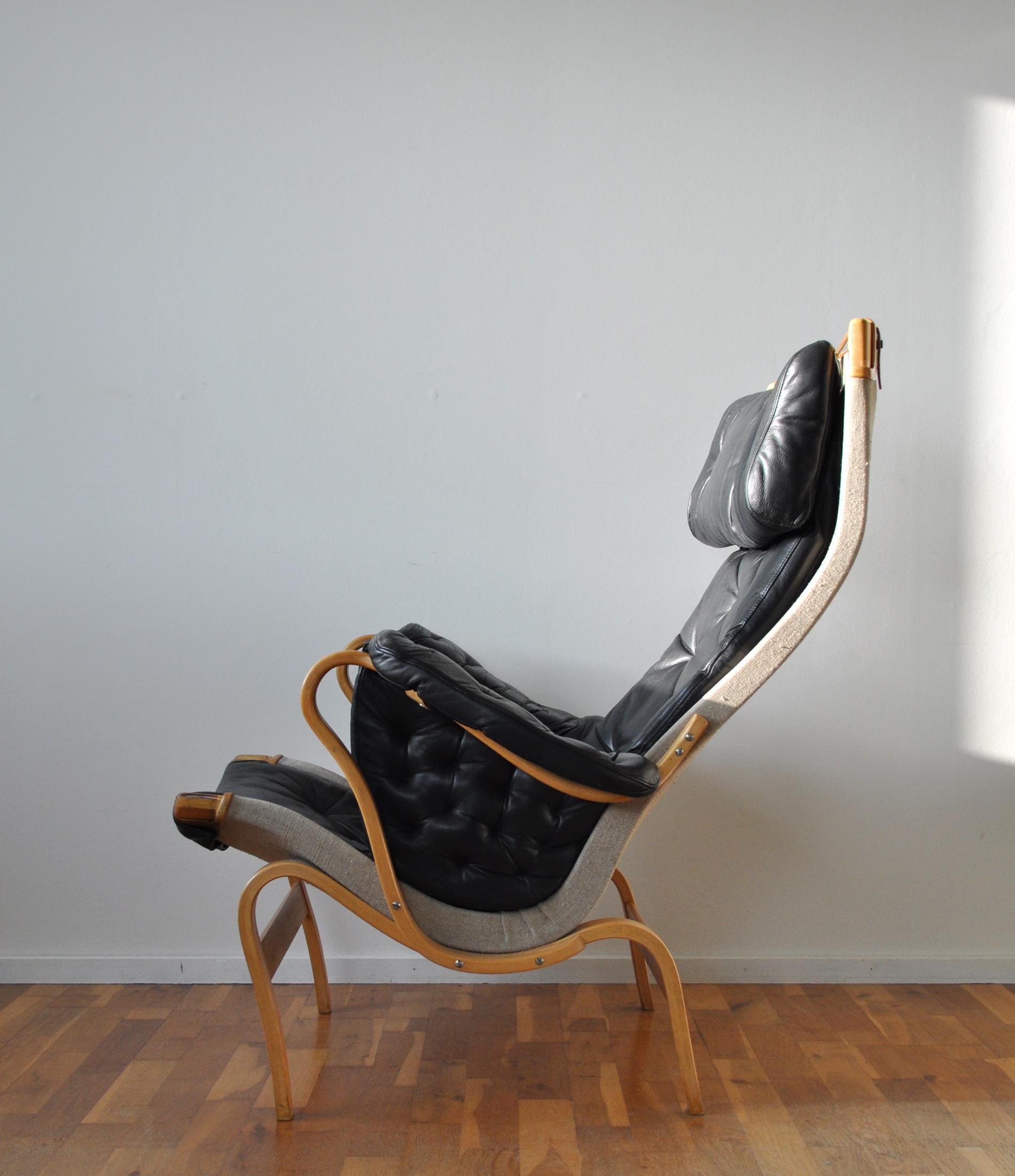 Comfortable Pernilla armchair designed by Bruno Mathsson. The first version was designed in 1944. This is an improved version designed for DUX in 1969. It comes with frame of moulded beech stretched with canvas and black leather in a good vintage