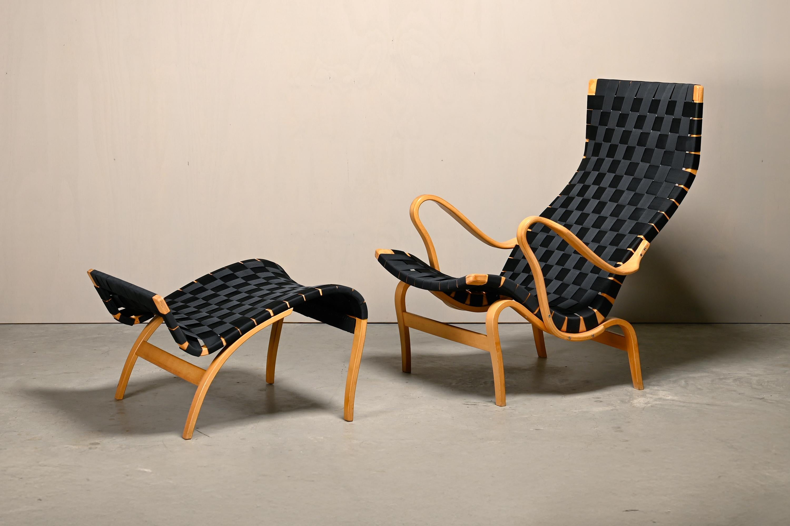 Iconica poltrona easy con ottomana disegnata da Bruno Mathsson nel 1944 e prodotta da Dux, Svezia. Telaio in legno di faggio curvato e teso con cinghie di nylon nero in ottime condizioni. Sia la sedia che lo sgabello sono firmati dal timbro del