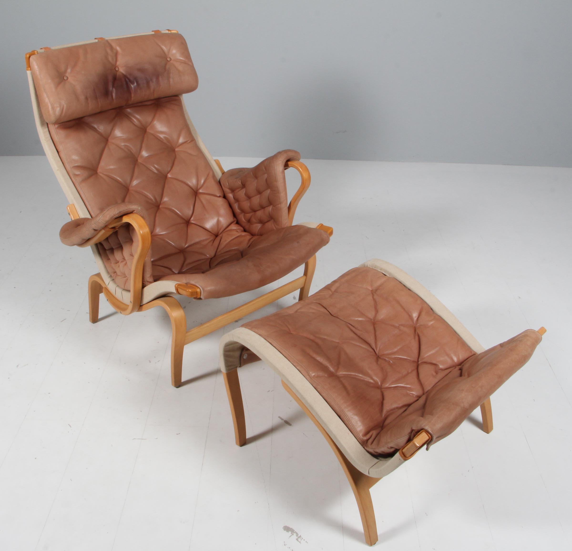 Bruno Mathsson Pernilla lounge chair with ottoman, original upholstery in patinated leather.

Frame in lacquered beech.

Made by DUX.

