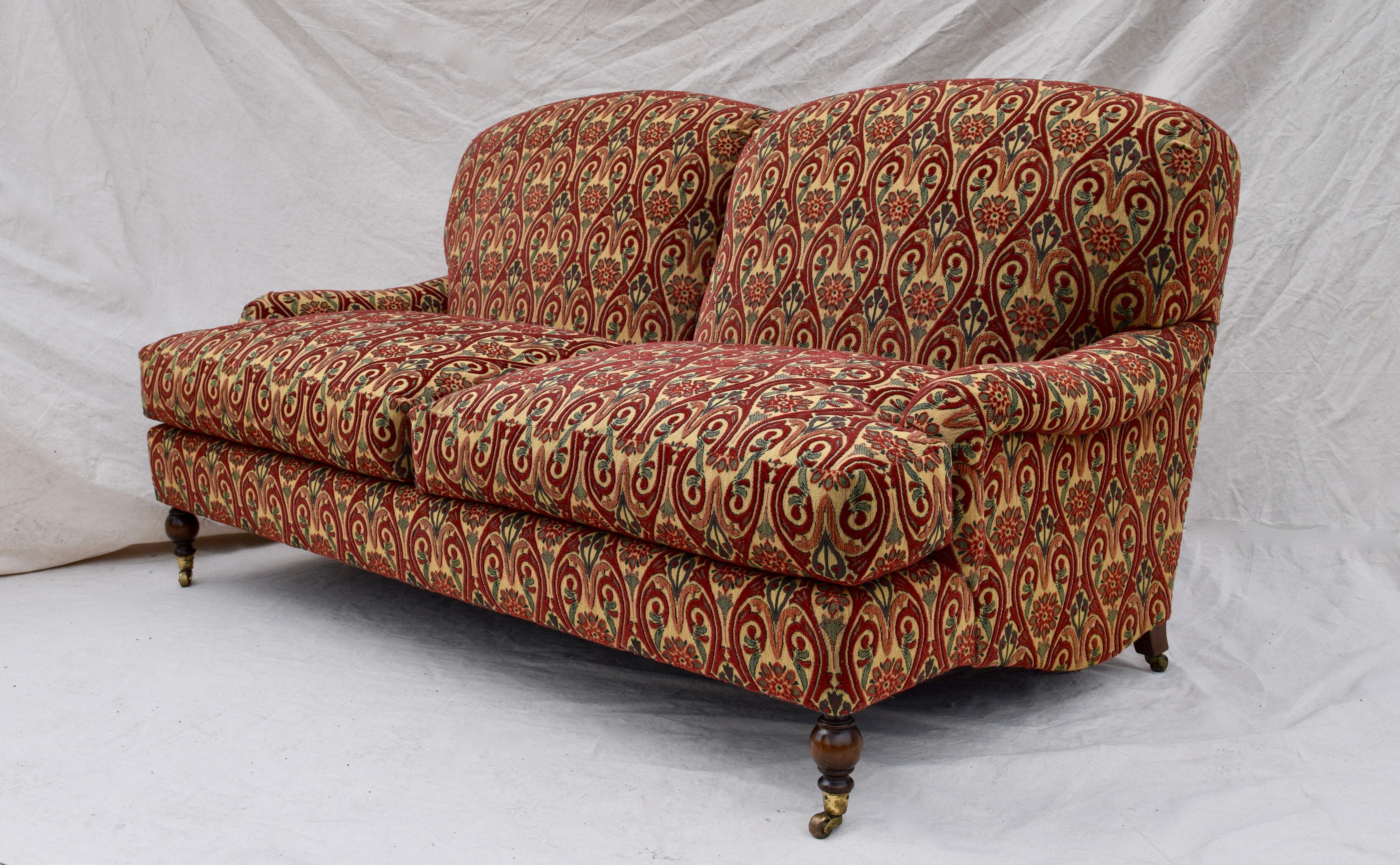 Luxurious two-seat sofa upholstered in lushly textured needlepoint tapestry style B & F fabric. Rolled arms, generously filled goose down cushions with turned mahogany front legs on brass castors are among many exceptional features offering an