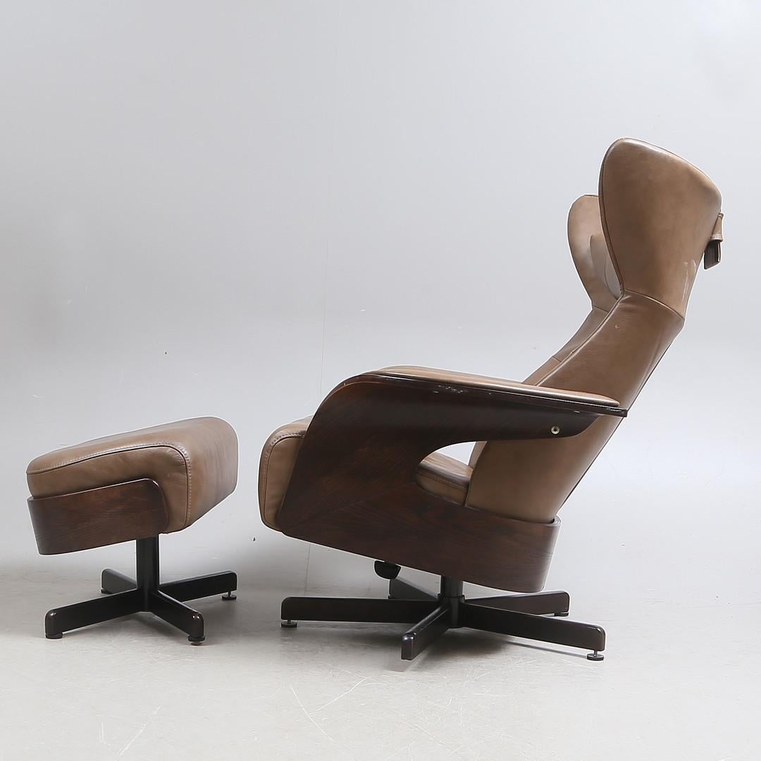 Leather and hardwood Amanda armchair with ottoman, foot crosses made of matte chrome-plated steel, swivel base. Loose neck pillow and seat cushion. Adjustable seat and back. Measures: H 100, W 82 cm. Made by Brunstad Møbler in Norway in the 1990s.