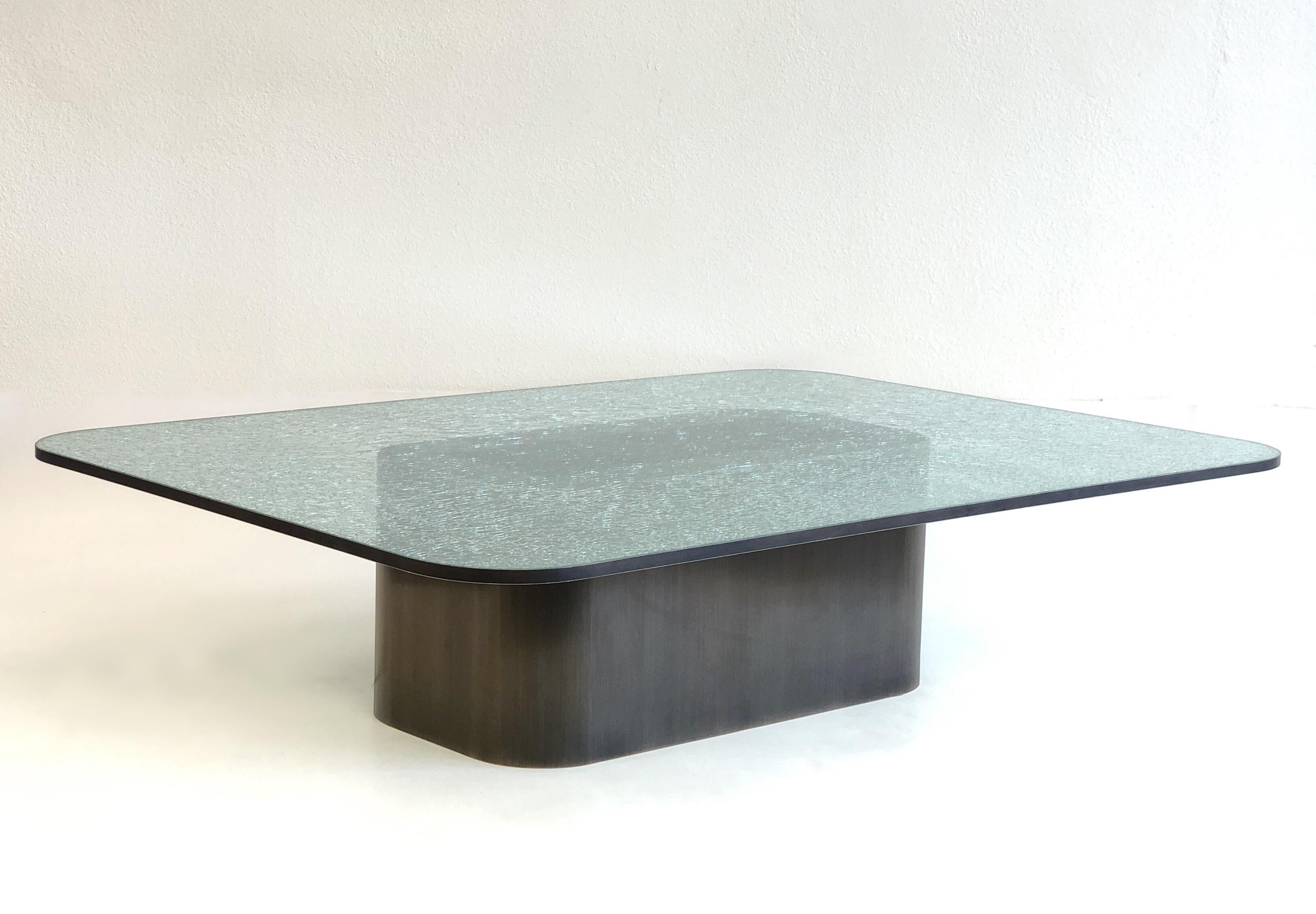 A spectacular 1980s large brushed bronze and crackle glass cocktail table by Renowned designer Steve Chase. 
The table base is brushed bronze and the top is 3/4” thick crackle glass with a brush bronze band around the edge. 
Minor wear on the top.