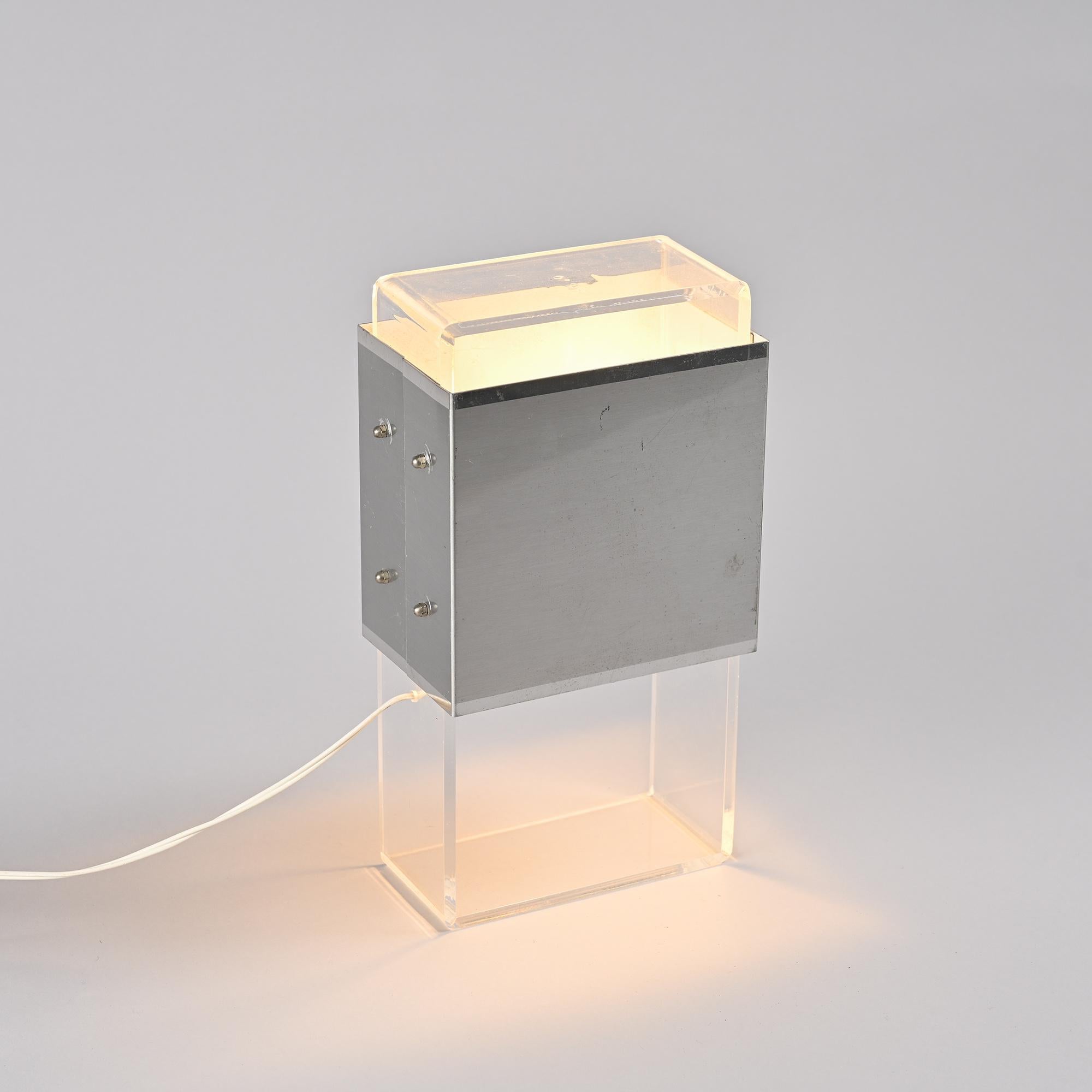 
Lampada da tavolo degli anni '70, nello stile di Philippe Jean, figura di spicco del design sperimentale francese dell'epoca.

Presenta una struttura in alluminio spazzolato che forma un volume geometrico minimo, intersecato da una fascia di