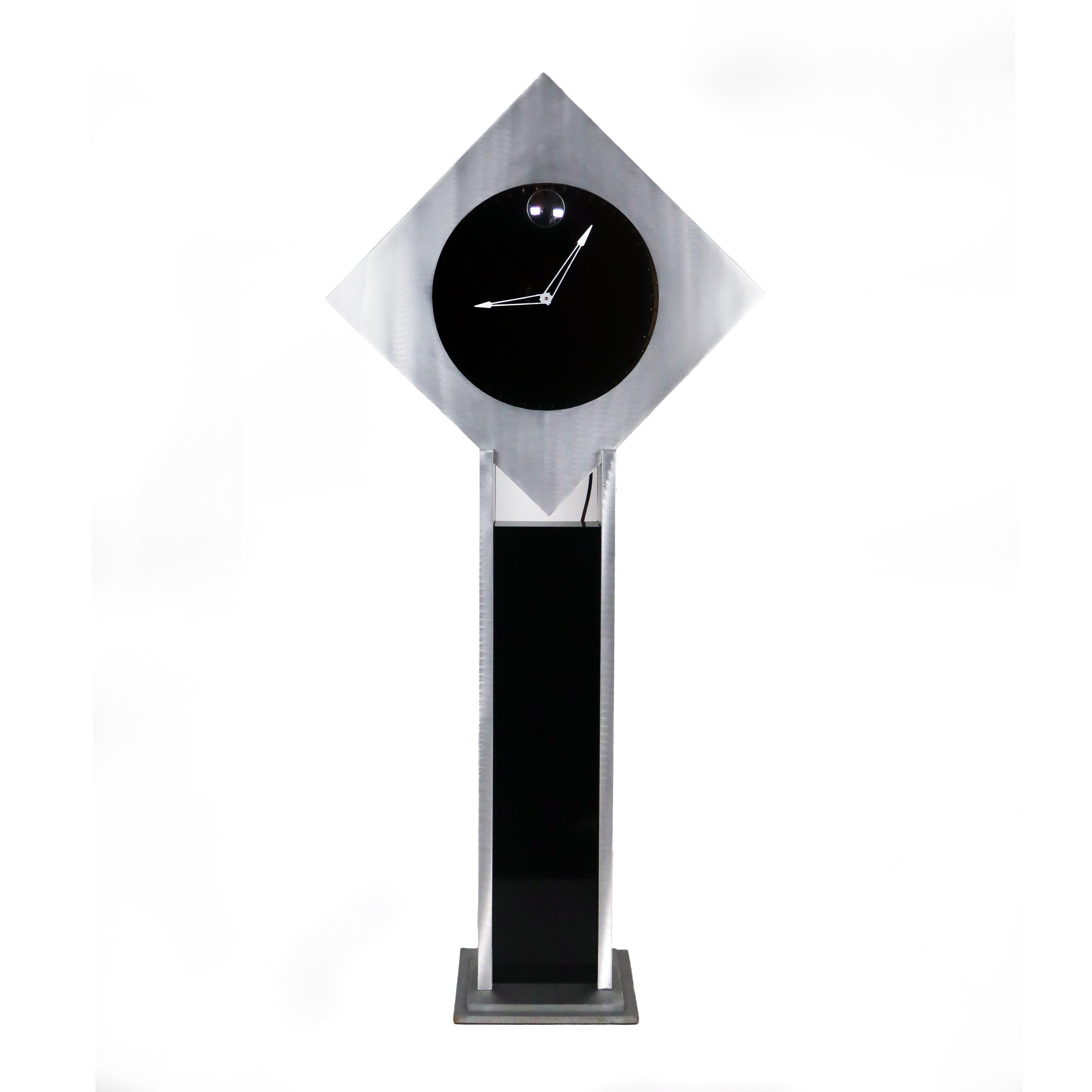 A unique and stunning diamond-shaped frame in brushed aluminum with two way mirrored clock face, mirrored interior, and infinity lighting. This modern design sits on a matching wood frame that is partially covered in brushed aluminum and partially