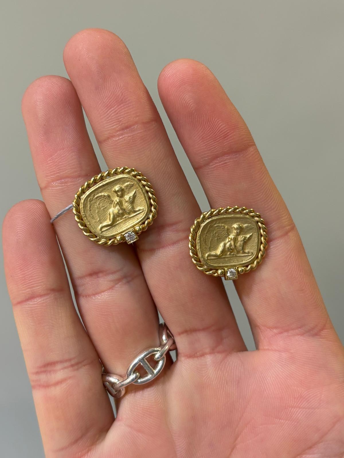 Orecchini in oro giallo 18 carati spazzolato e diamanti. Ogni orecchino raffigura un cherubino con le ali che tiene in braccio un animaletto. Gli orecchini sono delimitati da motivi a cordoncino in oro con un singolo diamante rotondo brillante