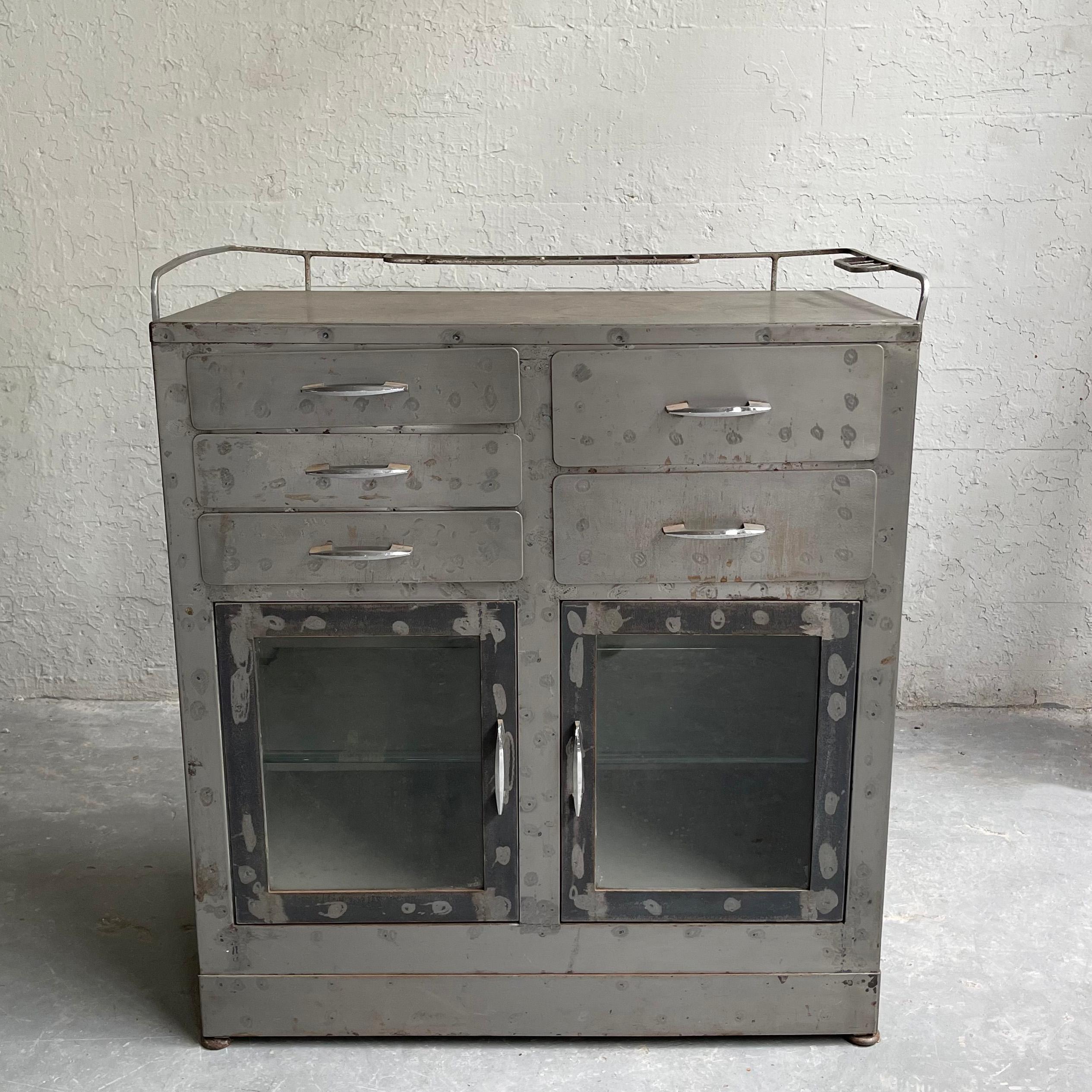 Early 20th century, industrial, brushed steel, apothecary cabinet, nurse station features top drawers, glass front bottom doors with glass interior shelves and an upper rack for bottles. Perfect as an industrial entryway piece or bar cabinet. The