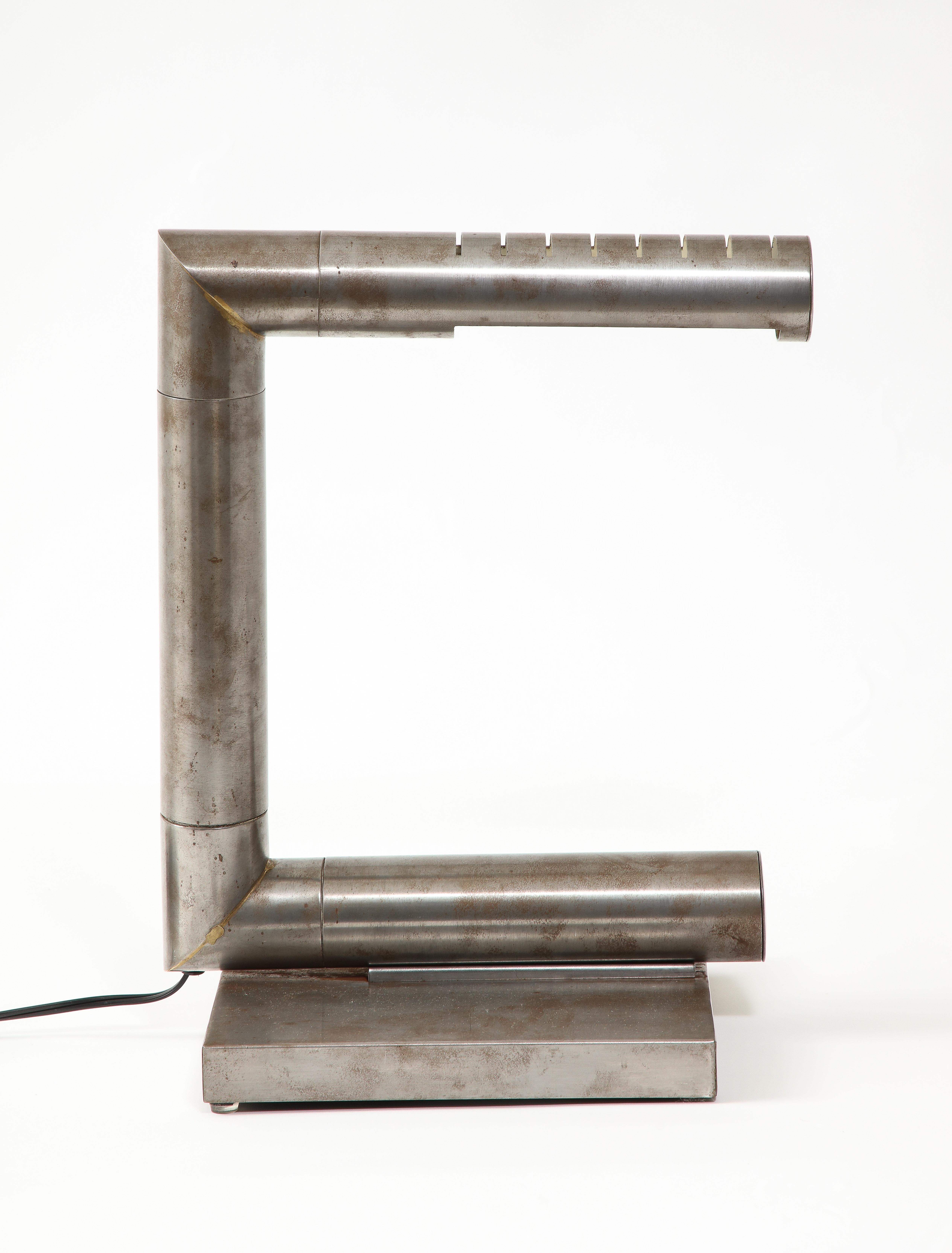 Schreibtischleuchte aus gebürstetem Stahl, in drei Richtungen verstellbar, mit quadratischem Sockel.

