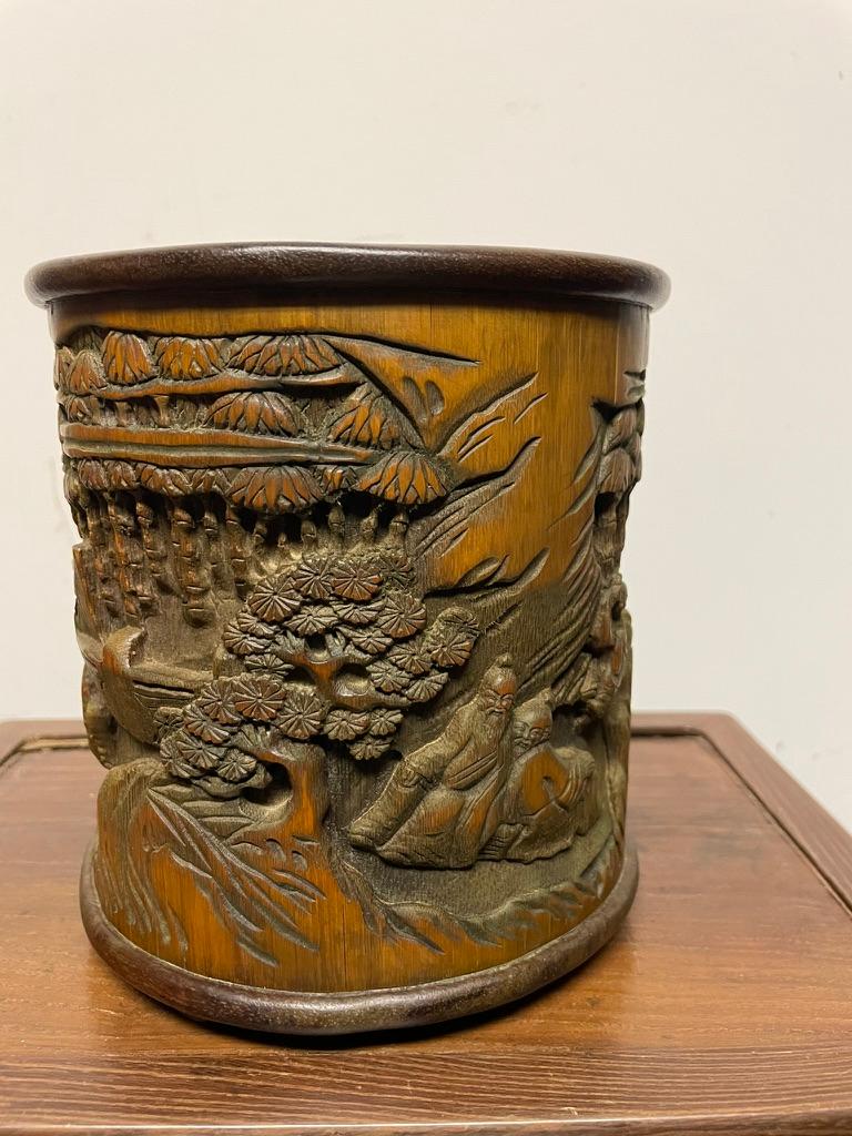 Chinese Ming style hand carved bamboo brush pot carved in the round with various scenes against the background of a bamboo forest. Two women make tea on a stove while two scholars sit at a table waiting. Three scholars are shown playing Go under a