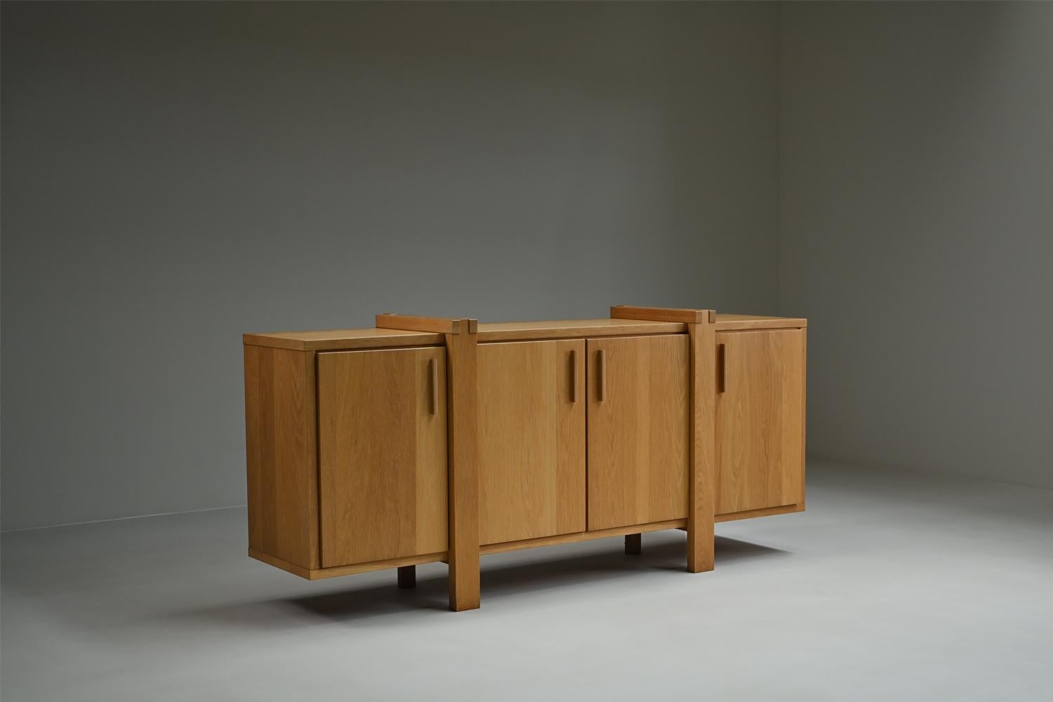 This Belgian sideboard is crafted mostly from solid oak and reflects the Brutalist style with its strong lines and architectural details. The piece offers plenty of storage with four cabinets. Its natural oak finish brings warmth and simplicity to
