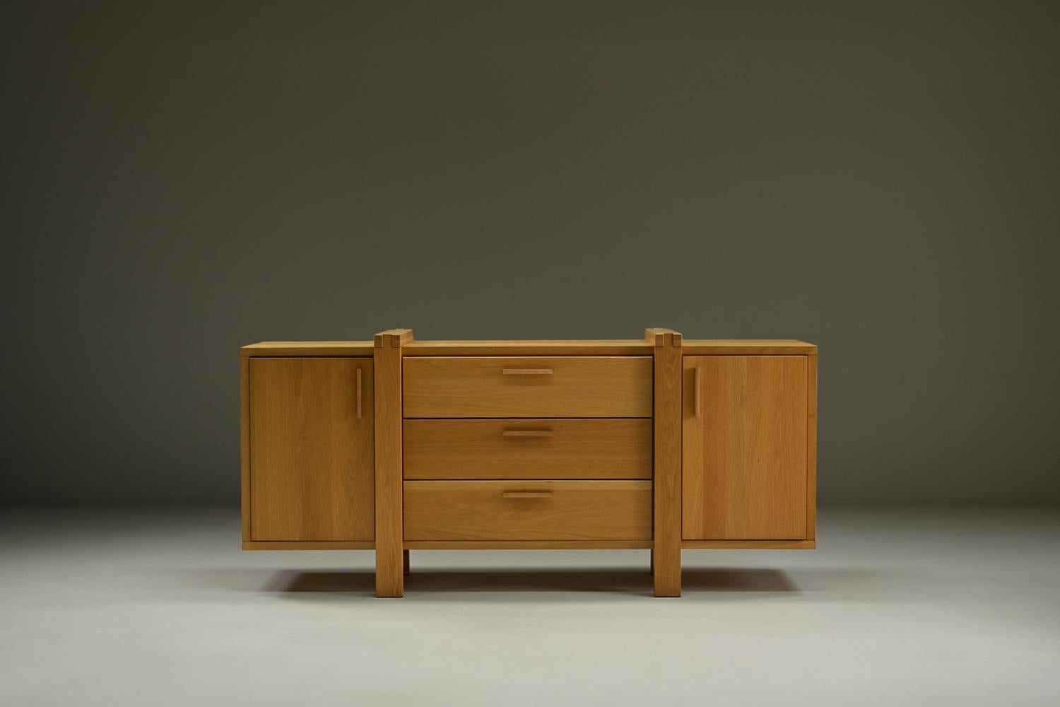 Questa credenza belga è realizzata principalmente in rovere massiccio e riflette lo stile brutalista con le sue linee forti e i suoi dettagli architettonici. Il mobile offre un ampio spazio di archiviazione con 2 armadi e 3 cassetti. La finitura in