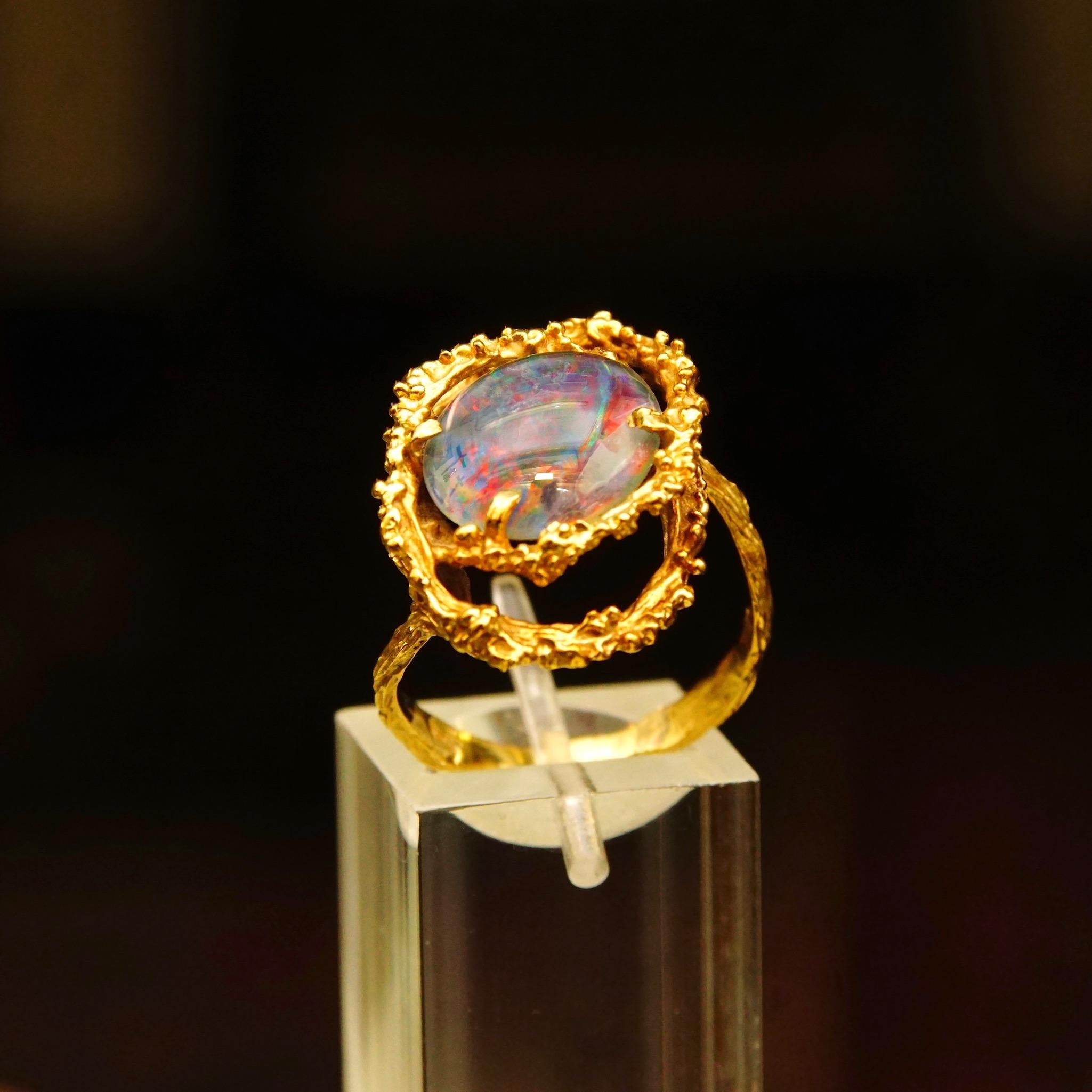 This absolutely stunning brutalist 14k yellow gold cocktail ring features a single focal genuine earth-mined oval cabochon of a Black Opal. The stone is secured in the middle of two interwoven ovals with organic prickled texturing and mounted on a