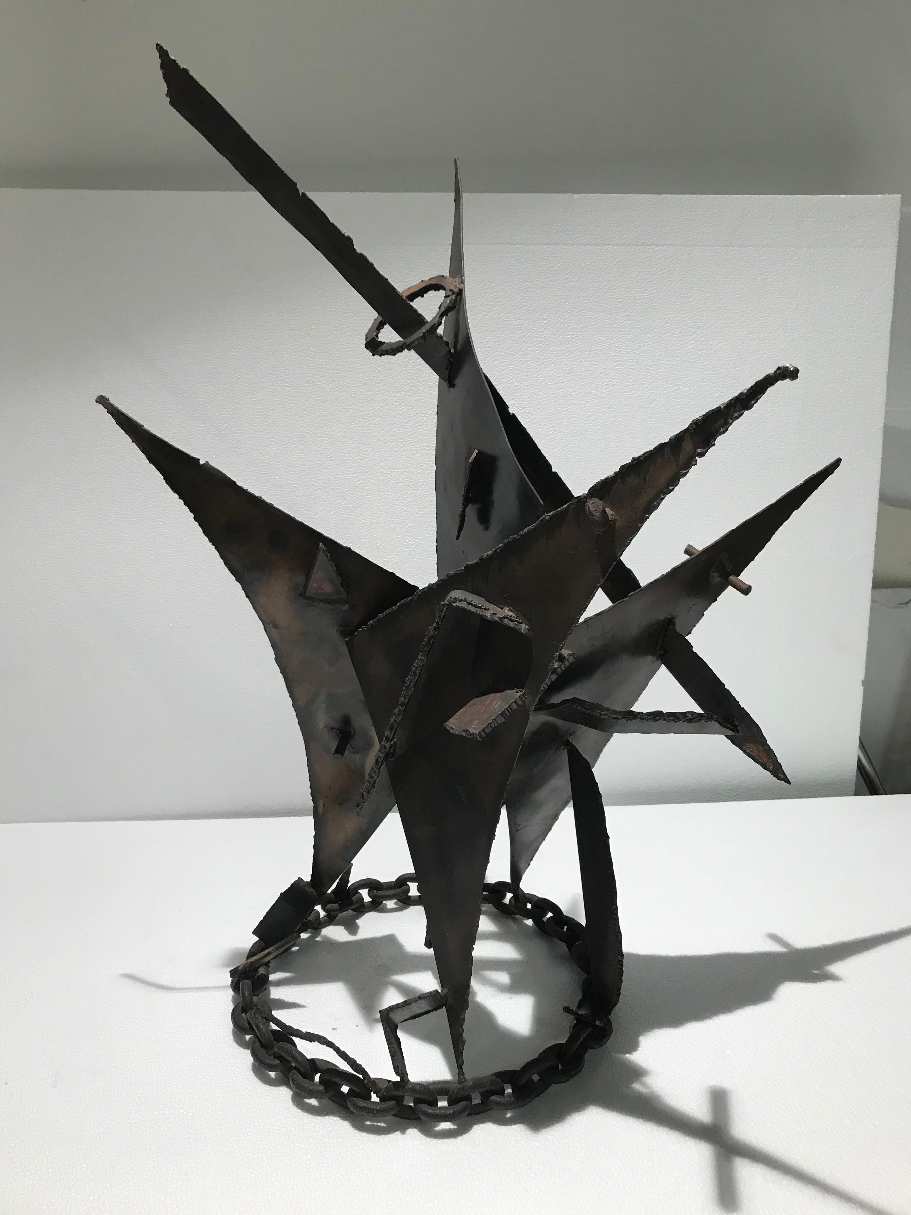 This sculpture, rendered in steel, is composed of 3 triangle shapes fused together and with spear piercing through its body. It has a thought-provoking circular rustic chain base. The abstract figure changes from every perspective and light and has