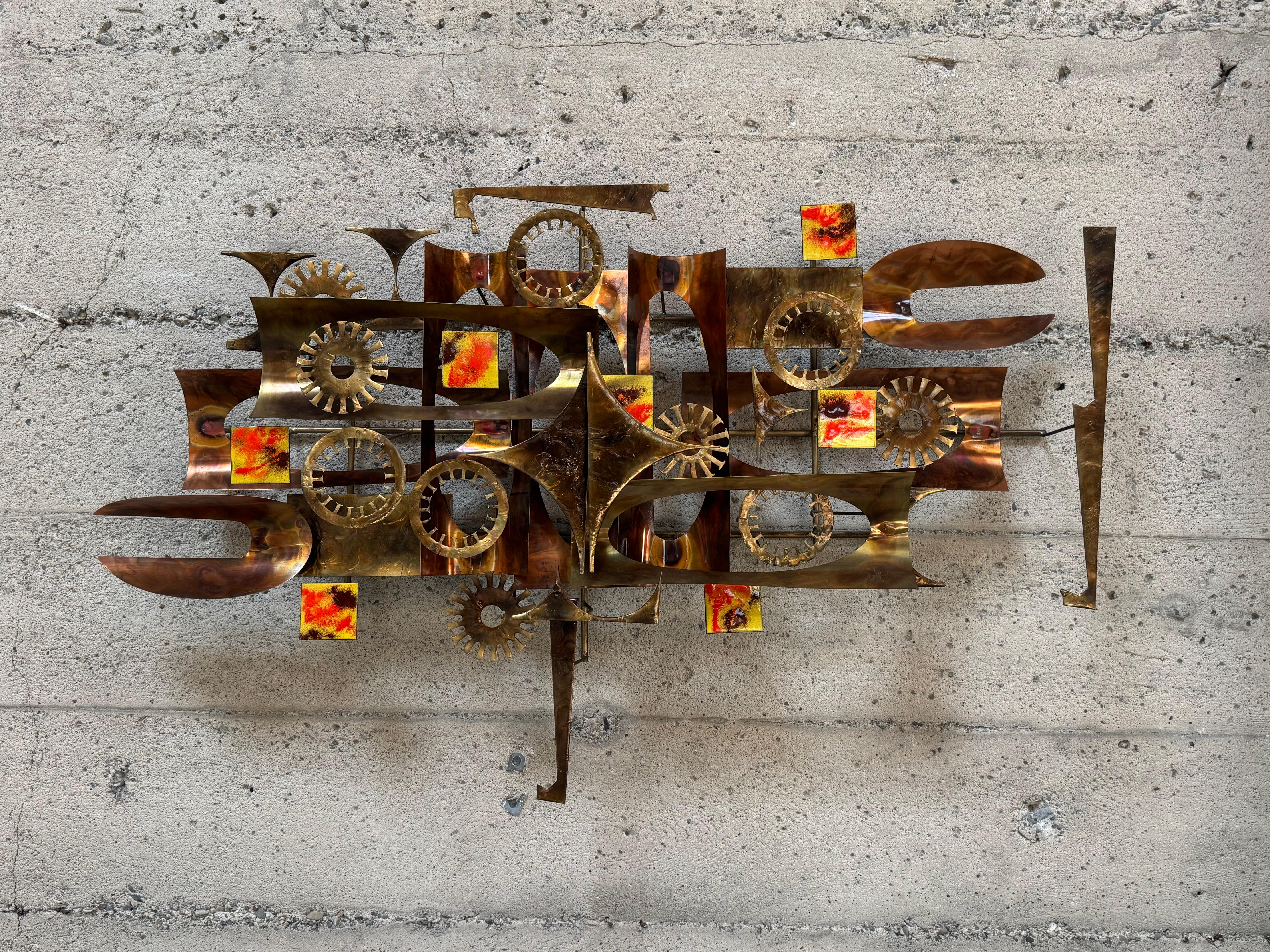 Abstrakte Wandskulptur von William Vose mit einer Mischung aus Messing und Bronze farbig  Metall und emaillierte Elemente in einem erdigen Gelb, Ziegelrot und Braun. In die Skulptur sind verschiedene abstrakte Formen eingearbeitet, die eine skurrile