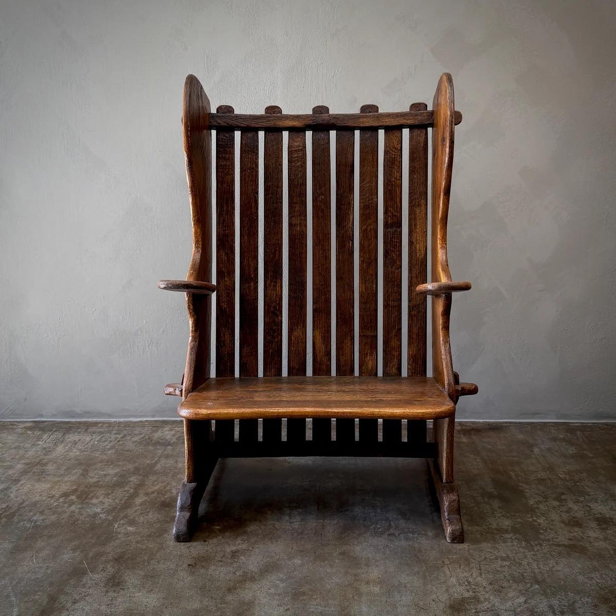 Dieser Sessel mit seiner robusten, kantigen Form und den freiliegenden Tischlerarbeiten ist ein Beispiel für die frühe Ästhetik des Brutalismus. Der aus dunklem, reich gemasertem Holz gefertigte Stuhl verfügt über eine hohe, gelattete Rückenlehne,