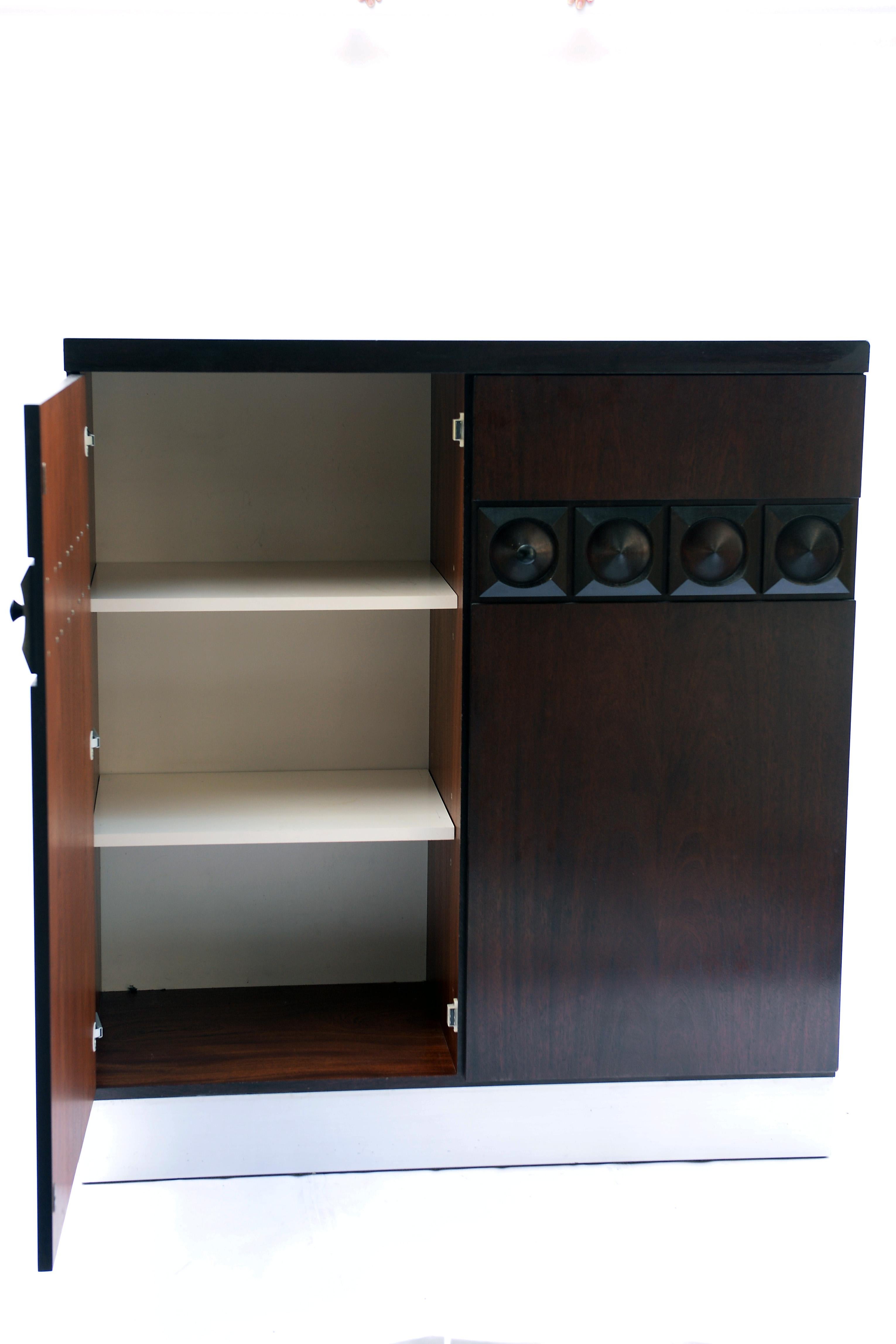 This two door cabinet is made from oak and unlike many other Brutalist cabinets this one has only a partly graphical design, making it more subtile.

It has two shelves on the left and the right door unveils a lit 3 shelves and a 3-bottle