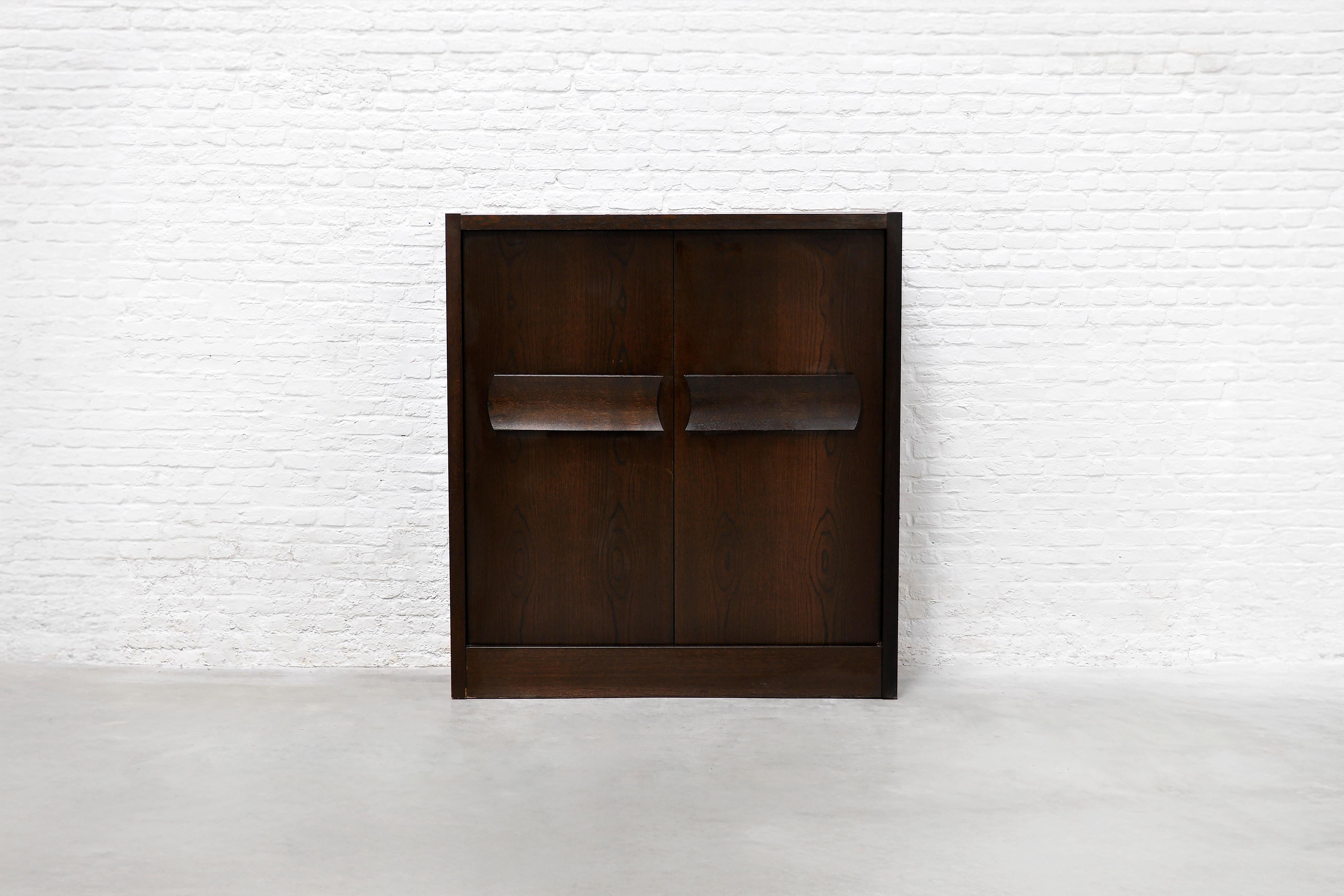 This striking Belgian bar cabinet from the 1970s showcases a raw, architectural aesthetic in dark-stained oak. Its bold, linear design is complemented by hand-bent oversized sculptural handles, adding a refined touch to its Brutalist character.
