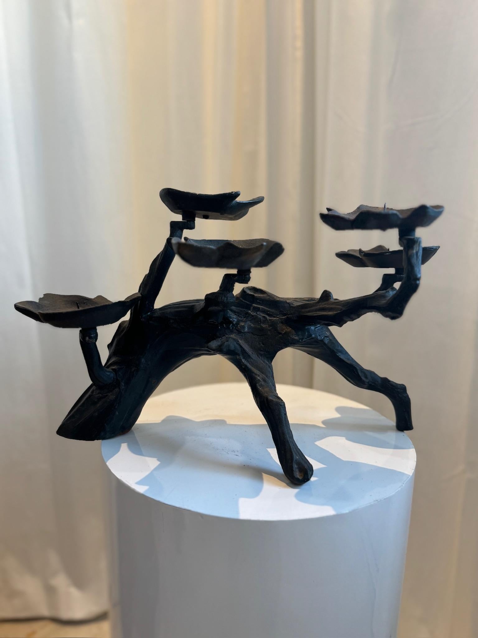 A striking Brutalist-style black iron candelabra featuring an organic, sculptural design with an intricate wood grain pattern. This handcrafted piece mimics the natural form of a twisted tree branch, offering a bold yet earthy aesthetic. With four