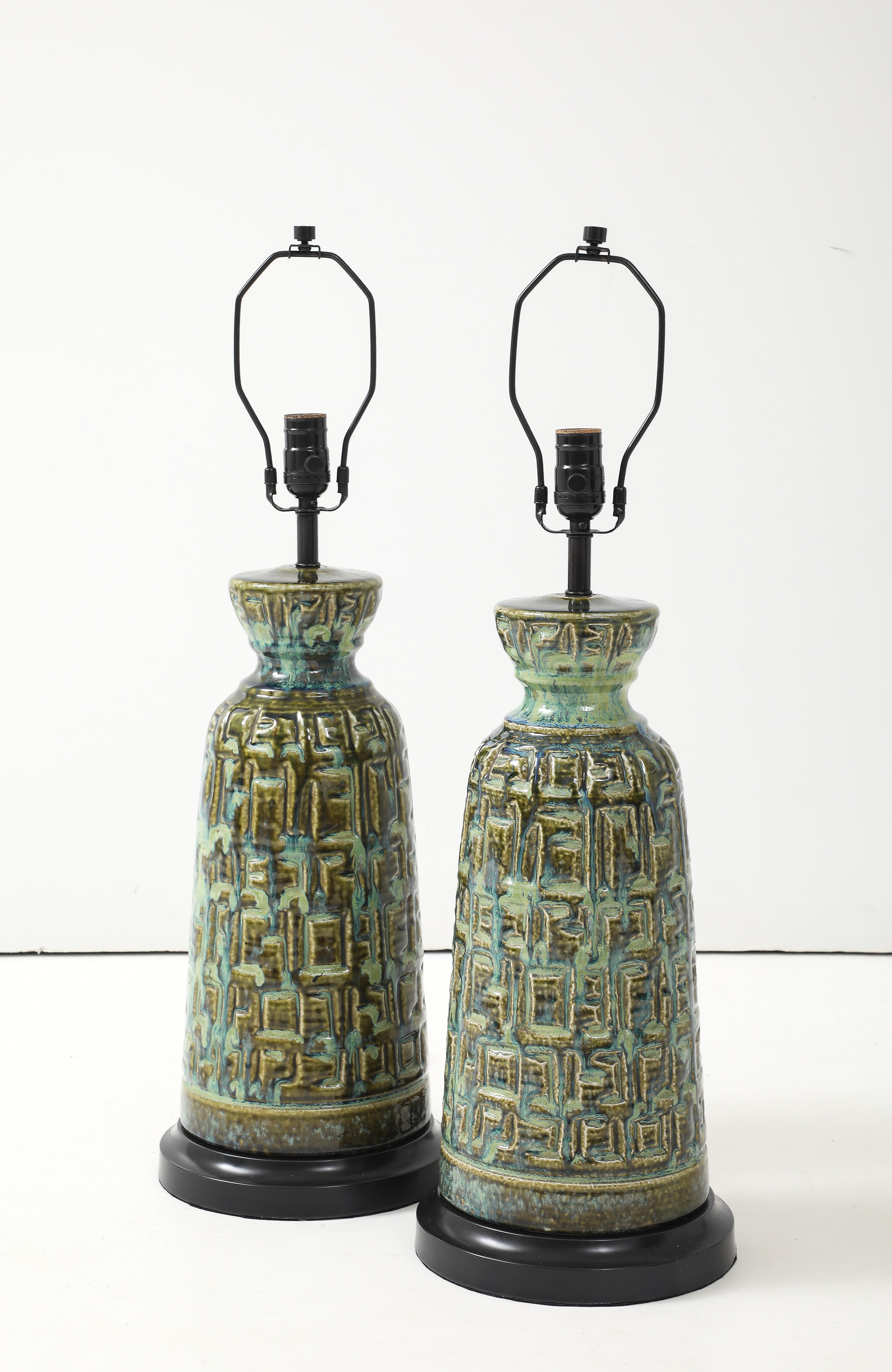 Pair of Brutalist porcelain lamps featuring a graphic raised pattern with a blue/green mottled glaze sitting on custom bronze bases. Rewired for use in USA. 