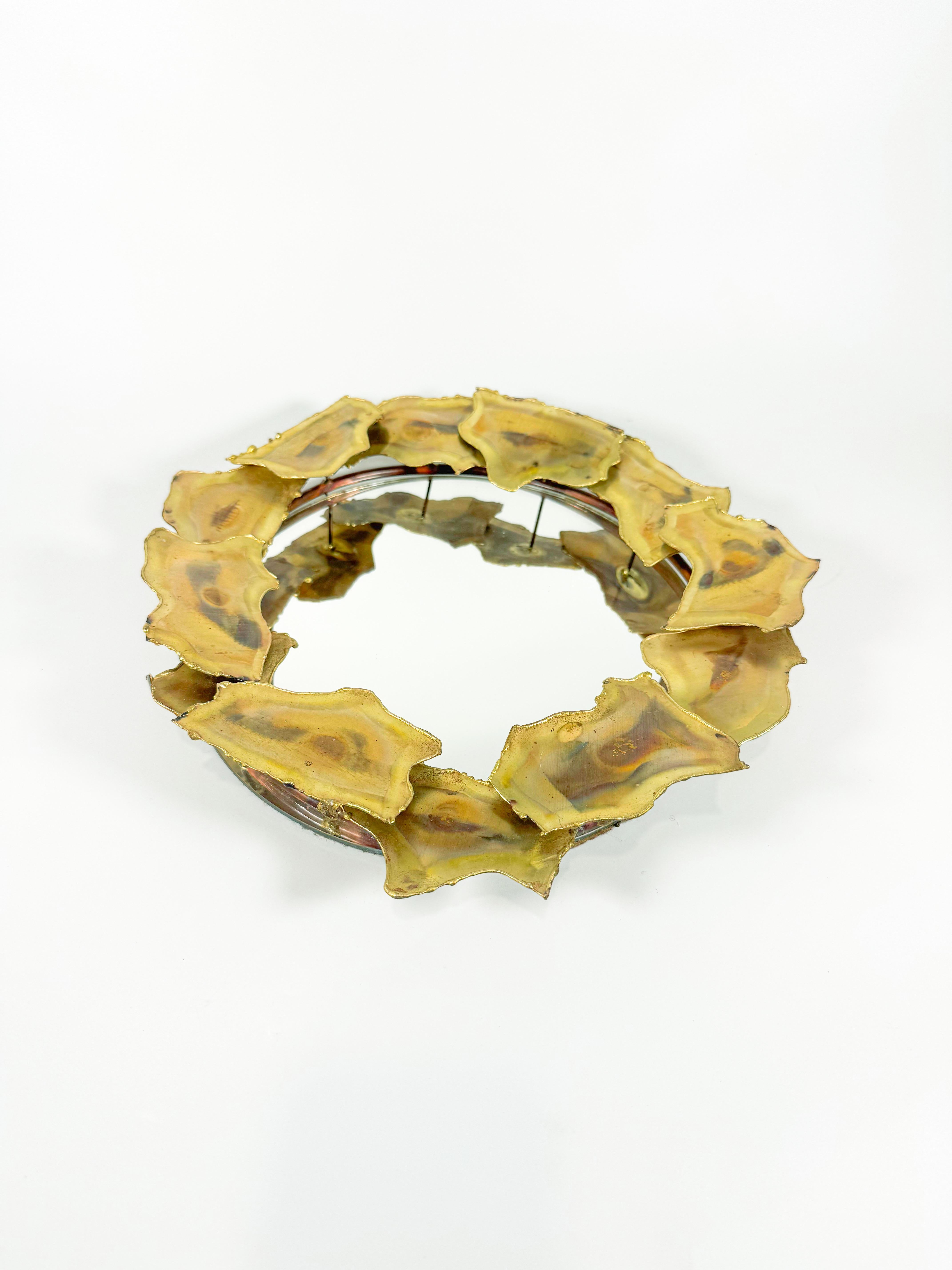 Un sorprendente specchio brutalista d'epoca realizzato a mano in Quebec negli anni '70. Questo pezzo scultoreo presenta piastre organiche in ottone tagliato a fiamma montate su una cornice circolare in rame, creando una texture dinamica e fusa che