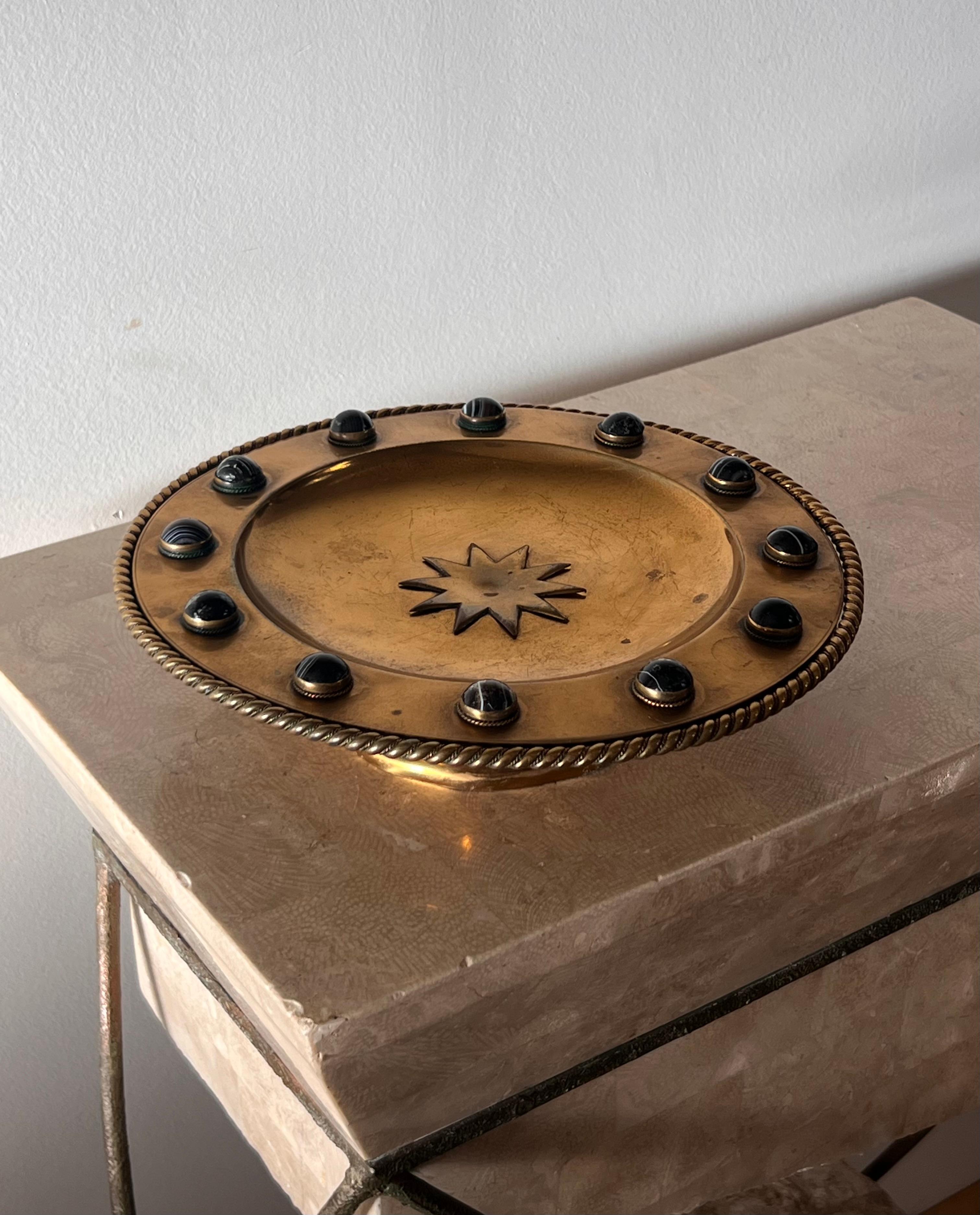 A bronze and copper hued brass platter or fruit bowl with braided edge, black onyx appliqués, and an embossed sun or star in center. Both Rococo and brutalist in temperament, this unique piece marries the hand-worked fastidiousness of brutalism with